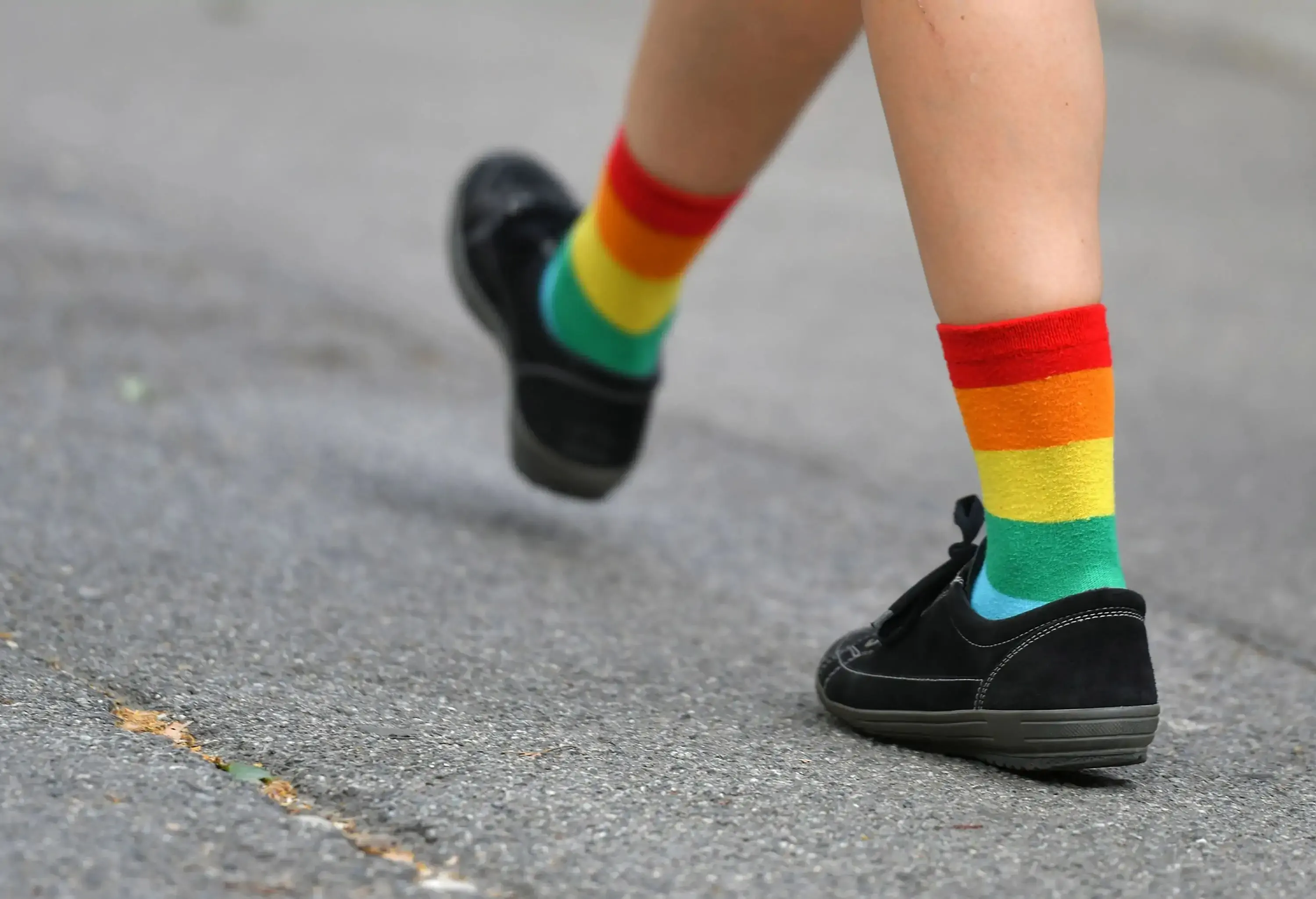 A person in black shoes and colourful socks walks down a street.