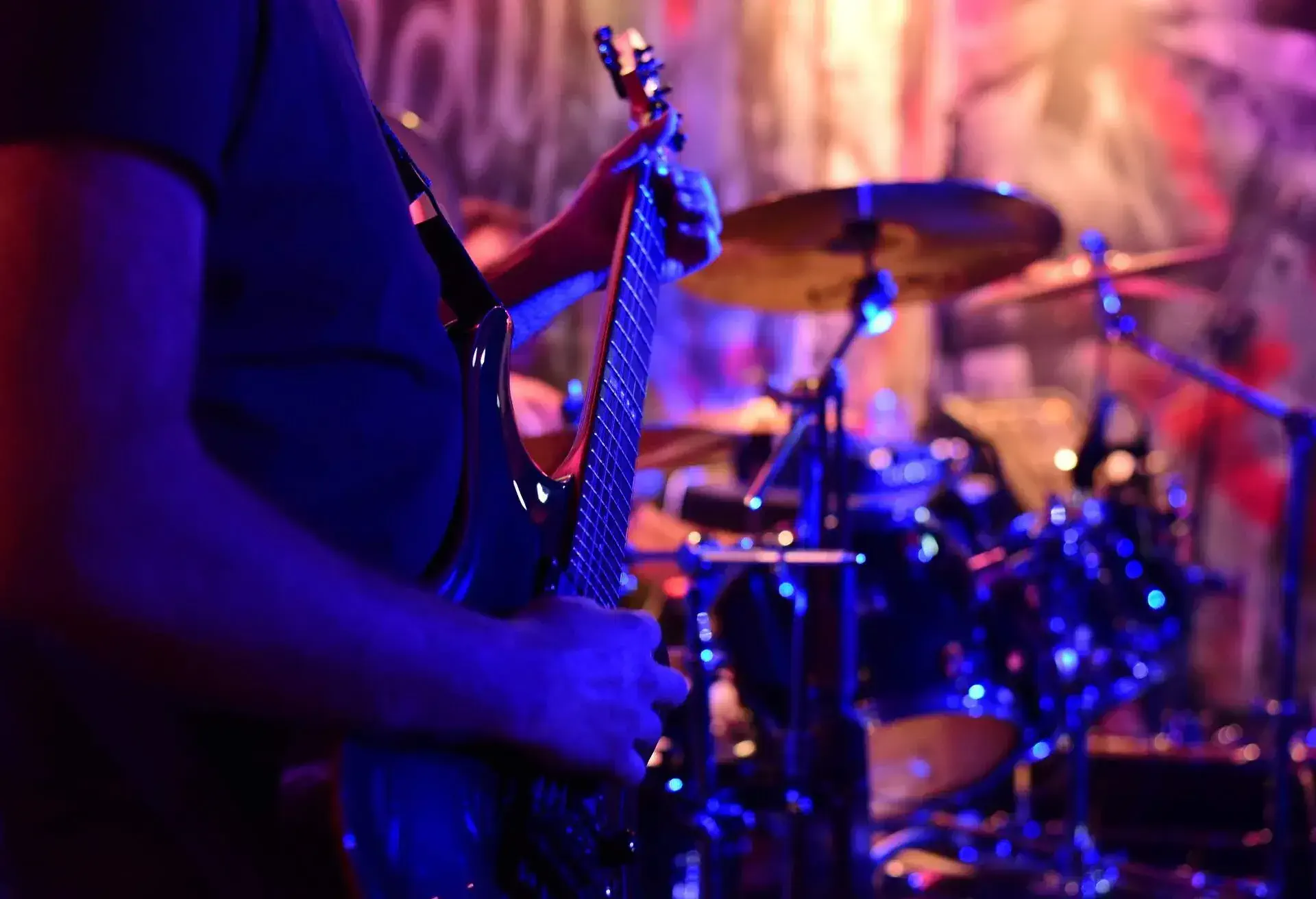 A person strumming a guitar next to a drum kit.