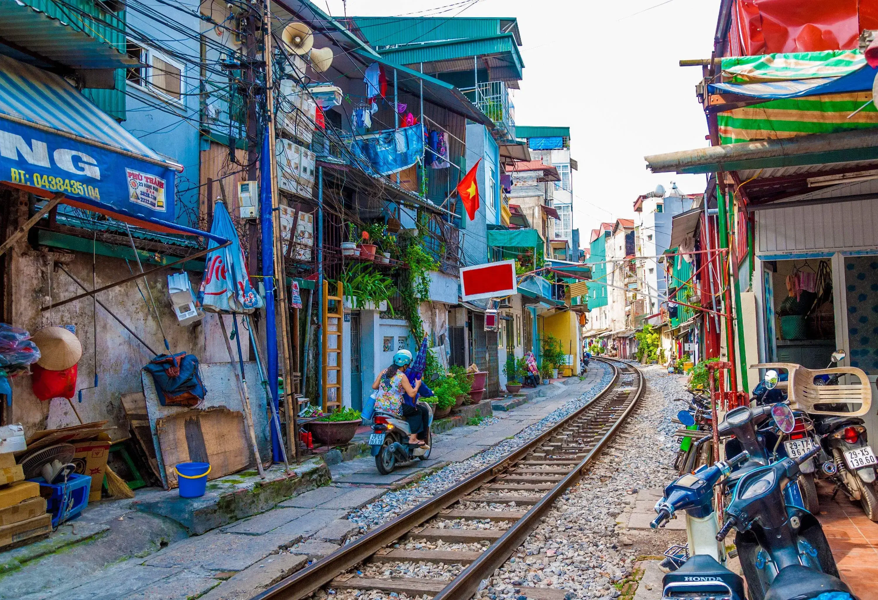 Tourists ride a motorcycle beside an empty railway across a residential neighbourhood.