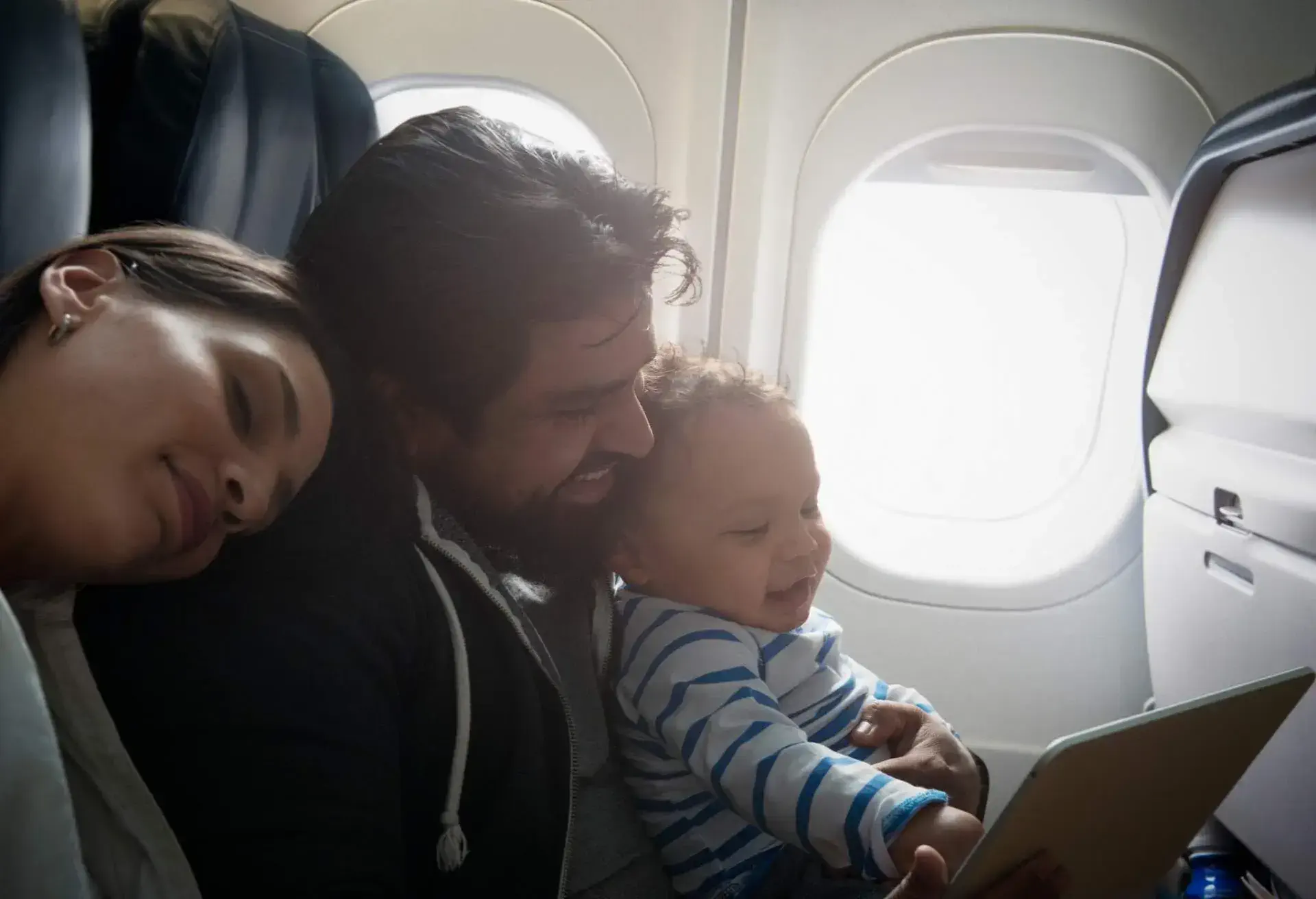 A baby sitting on a lap on a plane next to a window