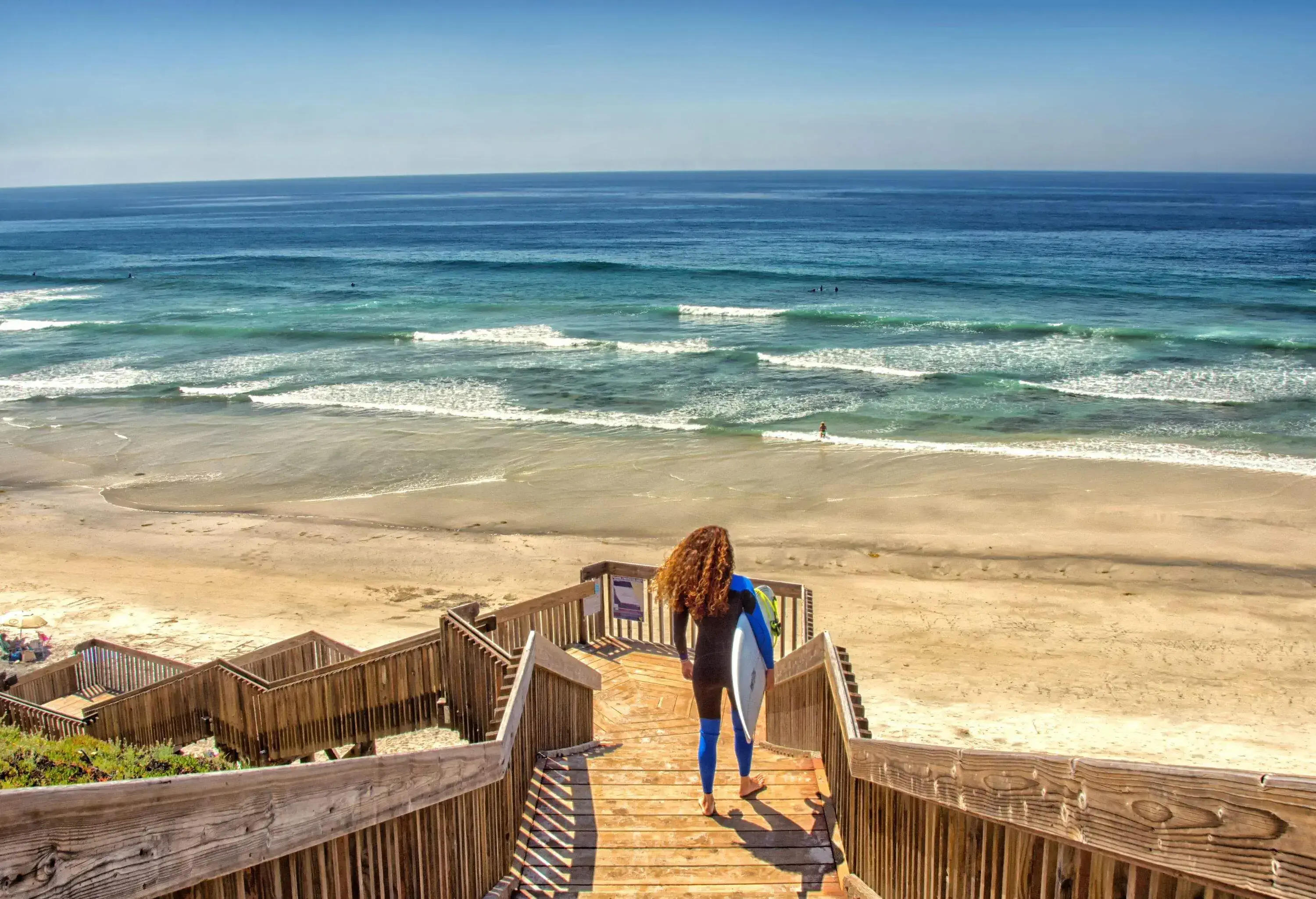Female surfer holding surfboard standing on wooden staircase looking at the sea