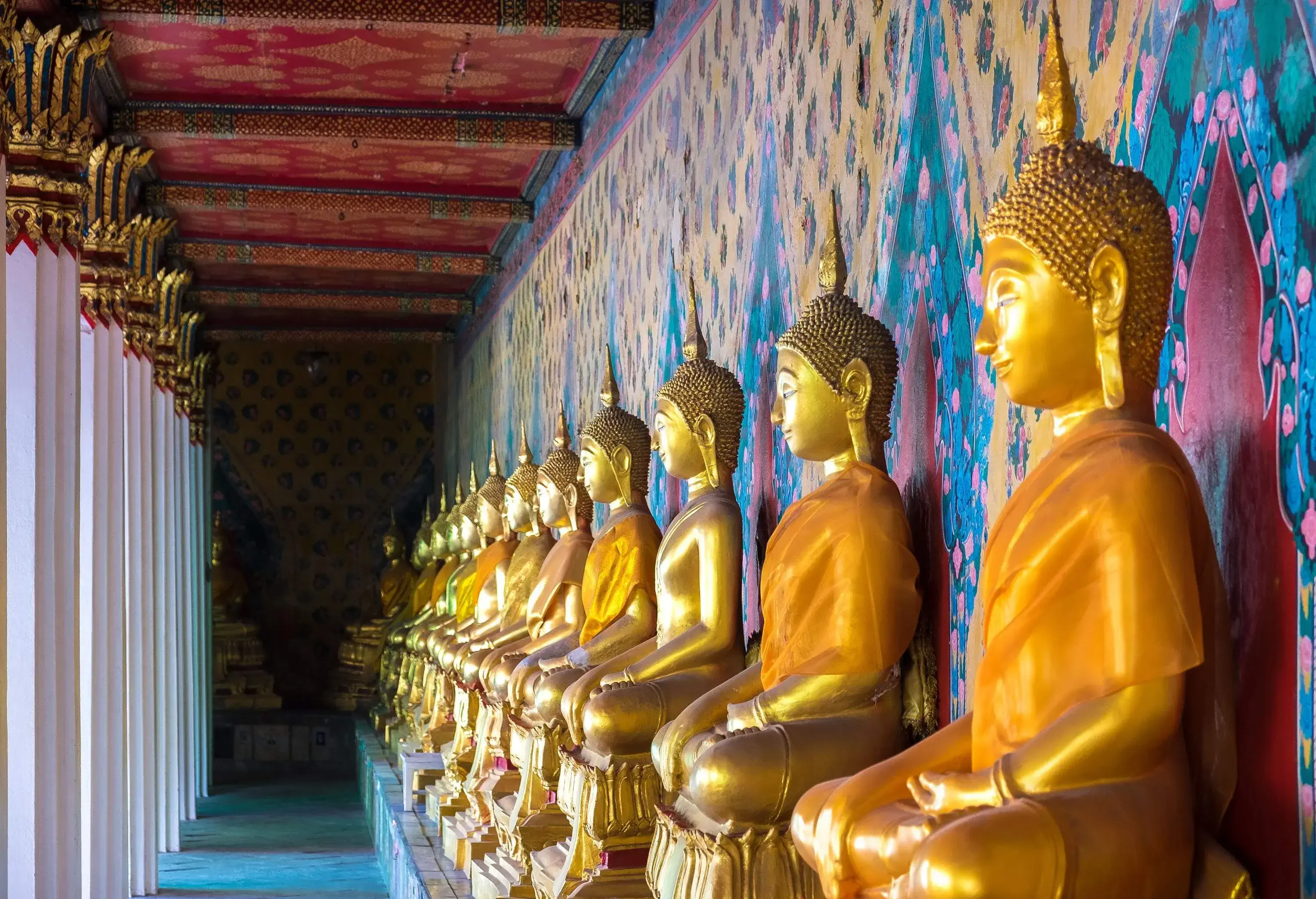 A line of golden Buddha statues seated cross-legged on a narrow alley.