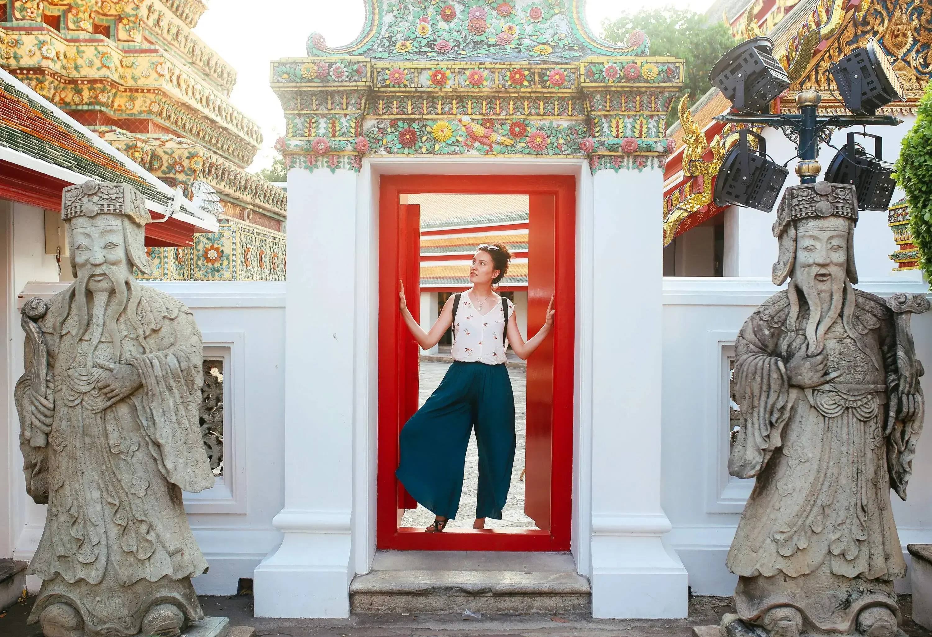 A tourist touches a red and white gateway surrounded by two concrete statues of elderly men with long beards.