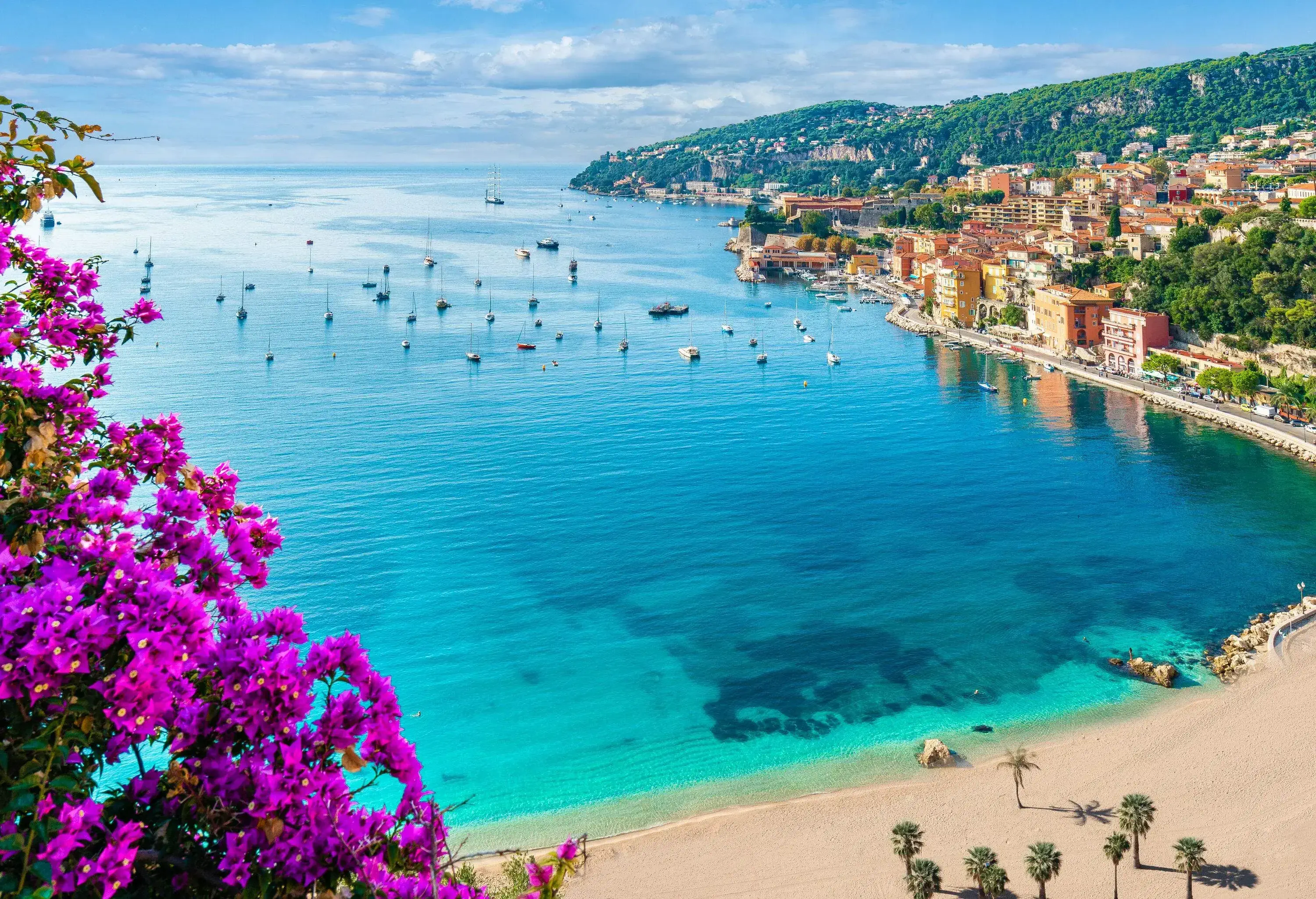 A picturesque view of the calm blue sea and a coastal and medieval town on a lush hill.