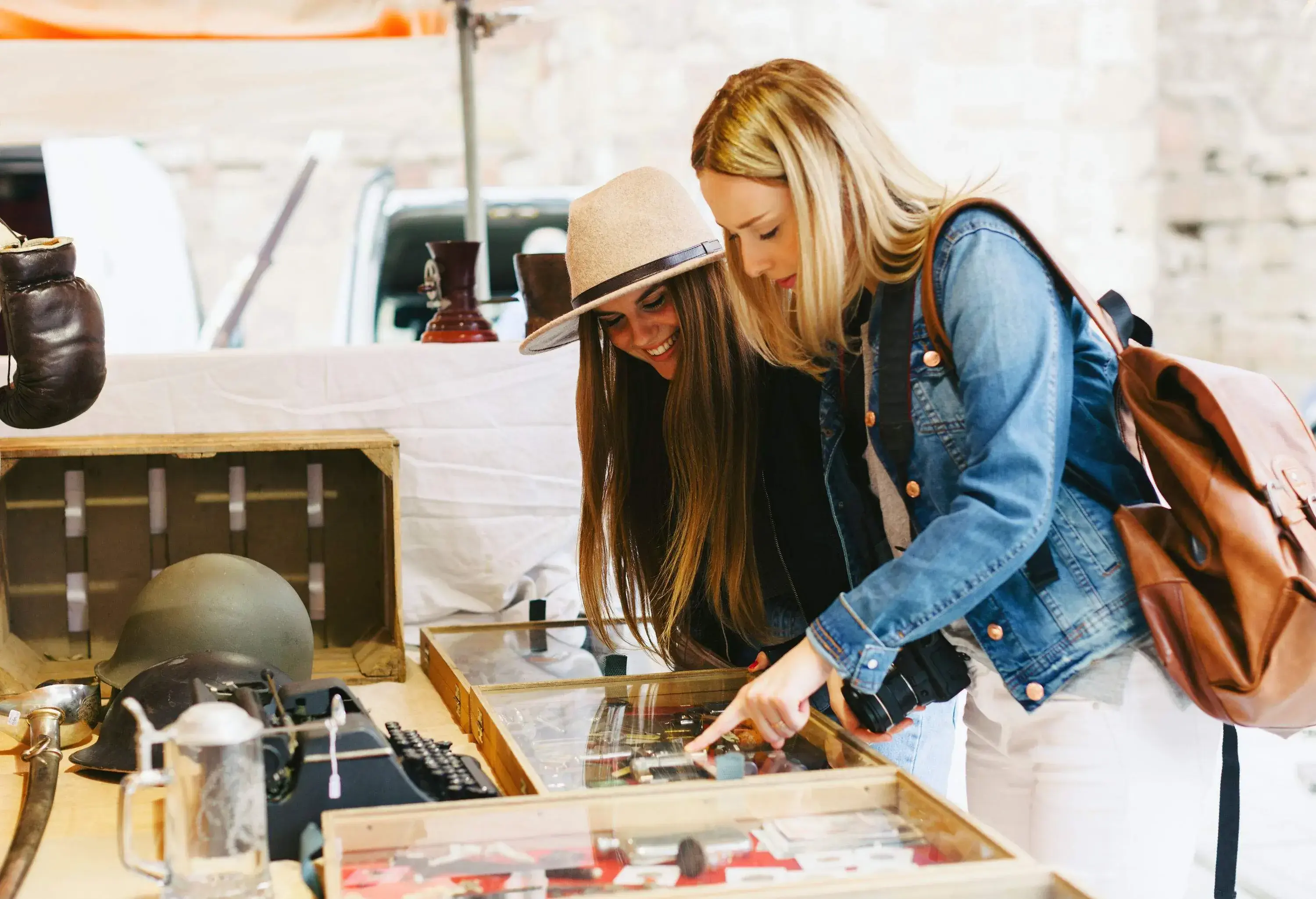 Two women in casual clothes look at glass-enclosed souvenirs displayed on a table, with one pointing at an item.