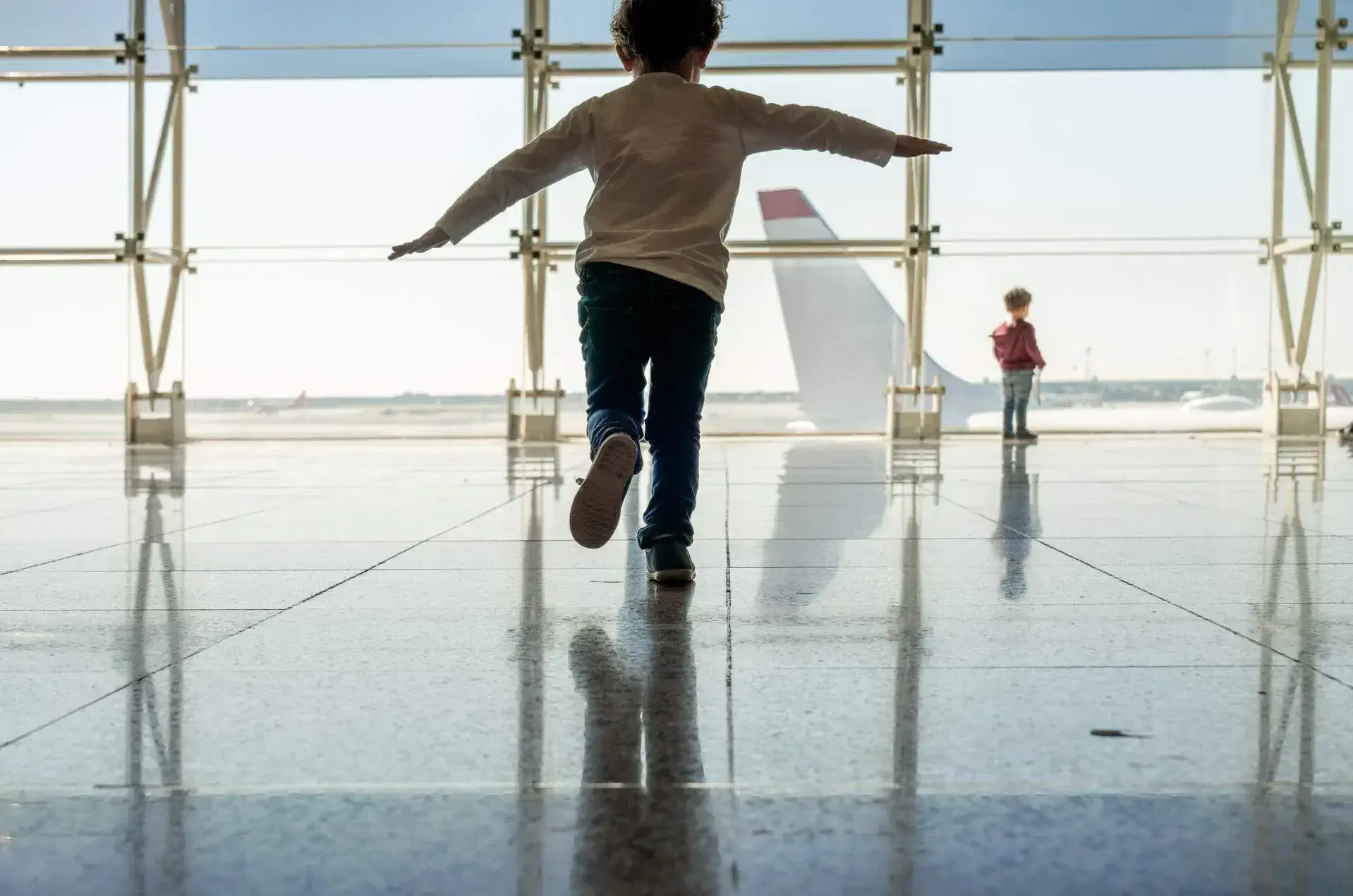 A kid running at the airport next to an airplane landing