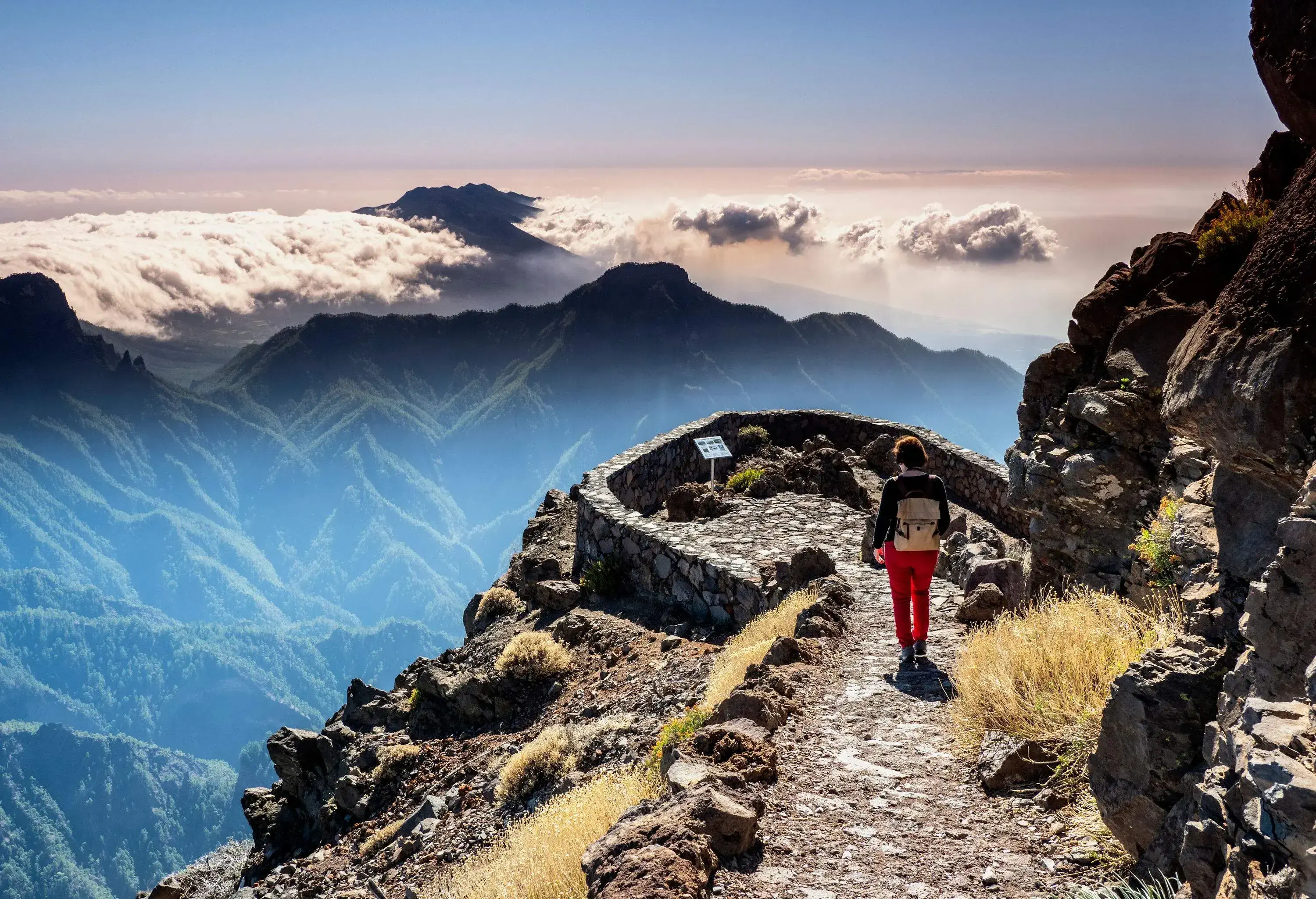 A woman walking towards a lookout terrace overlooking a cloud-capped mountainscape.