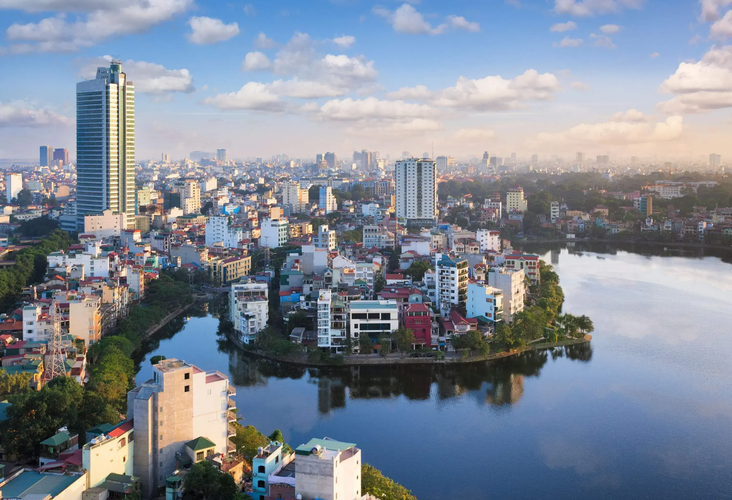 A dense cityscape with buildings and trees on the areas around a lake.