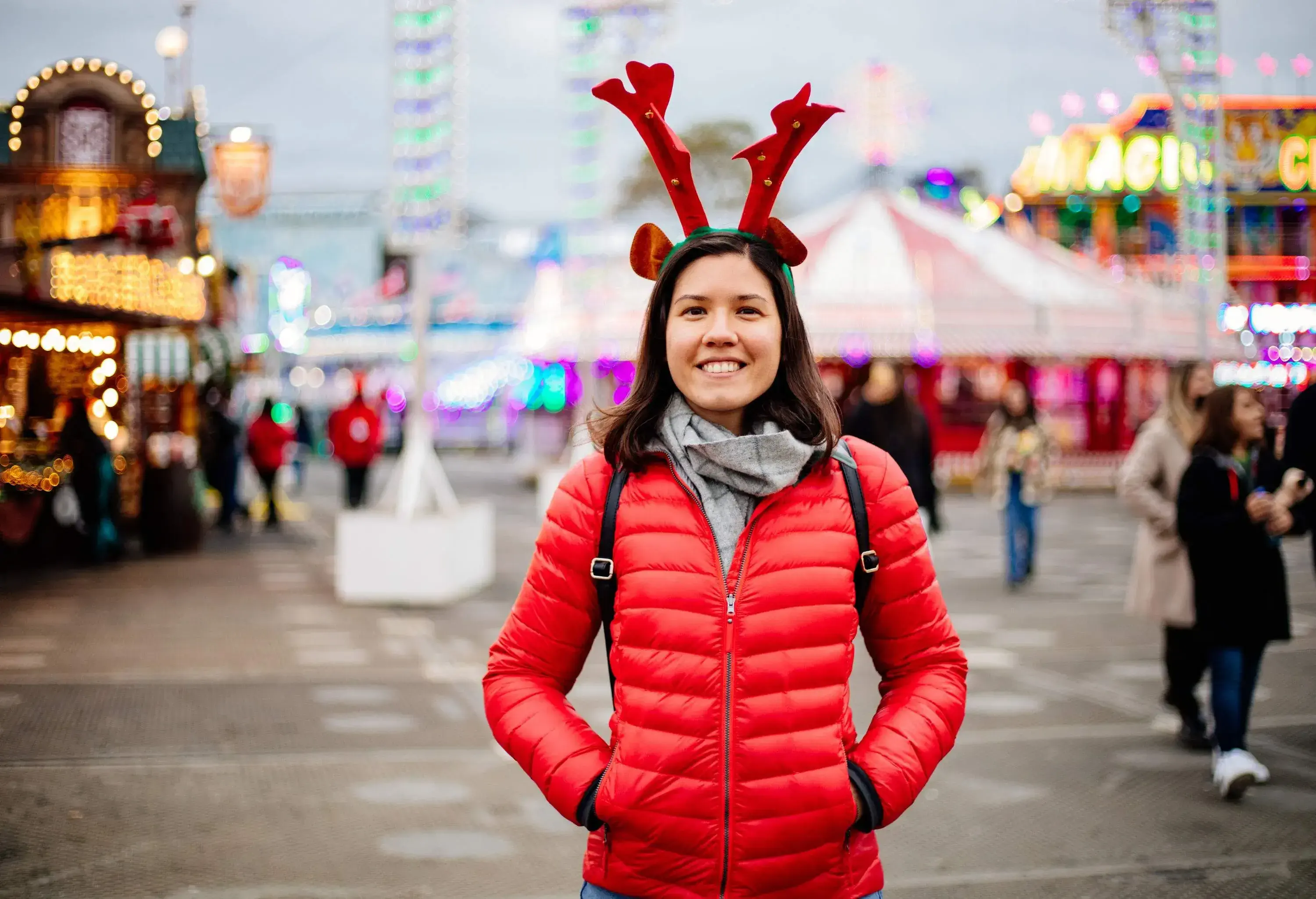 Happy woman wearing red jacket and antlers at the Christmas market in London during the day