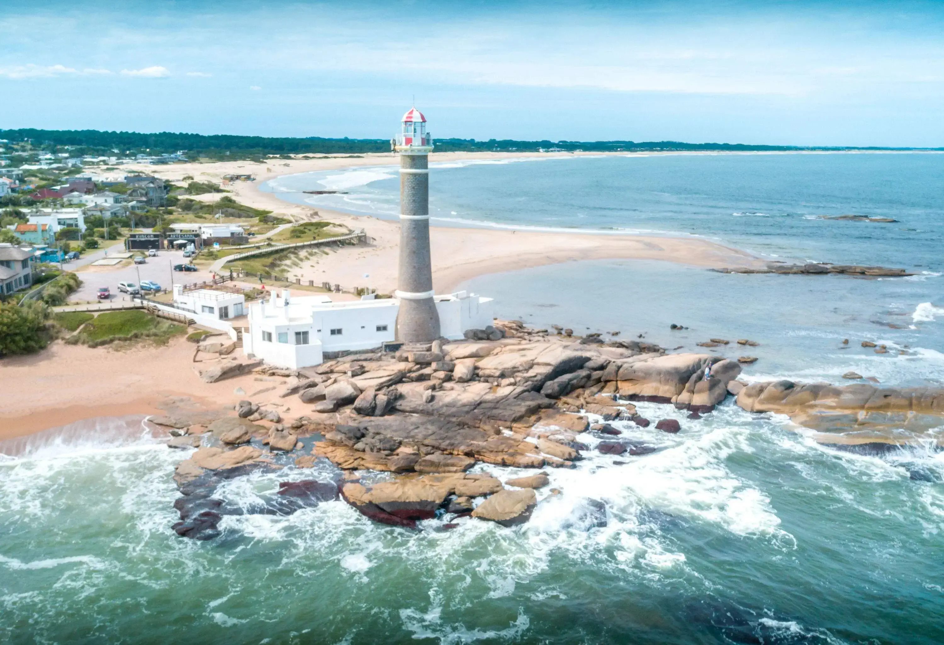 A lighthouse standing on a jumble of smooth sea rocks battered by the waves.