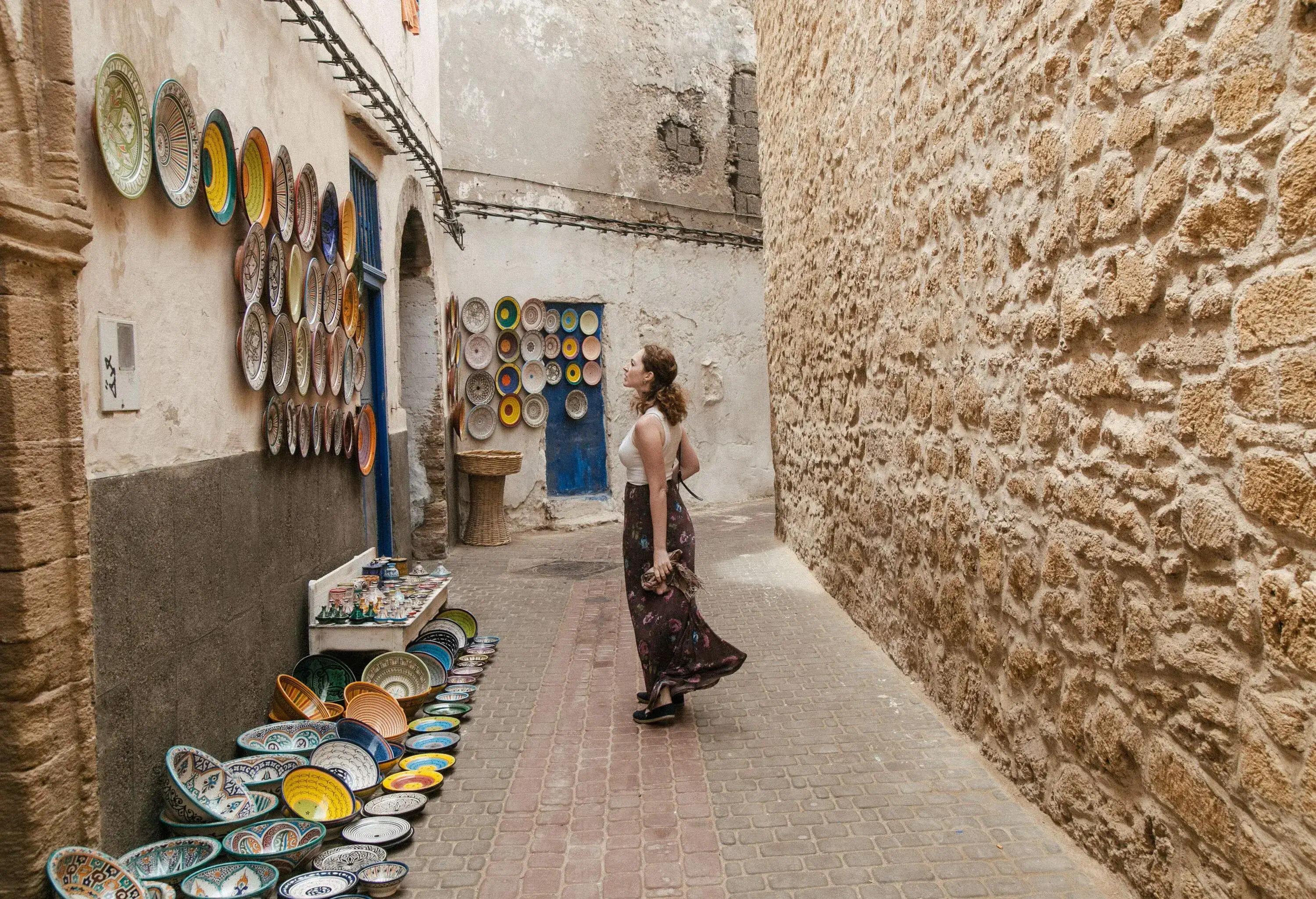 In a quaint alley, a person stands captivated, gazing at a collection of intricately designed plates adorning a wall.
