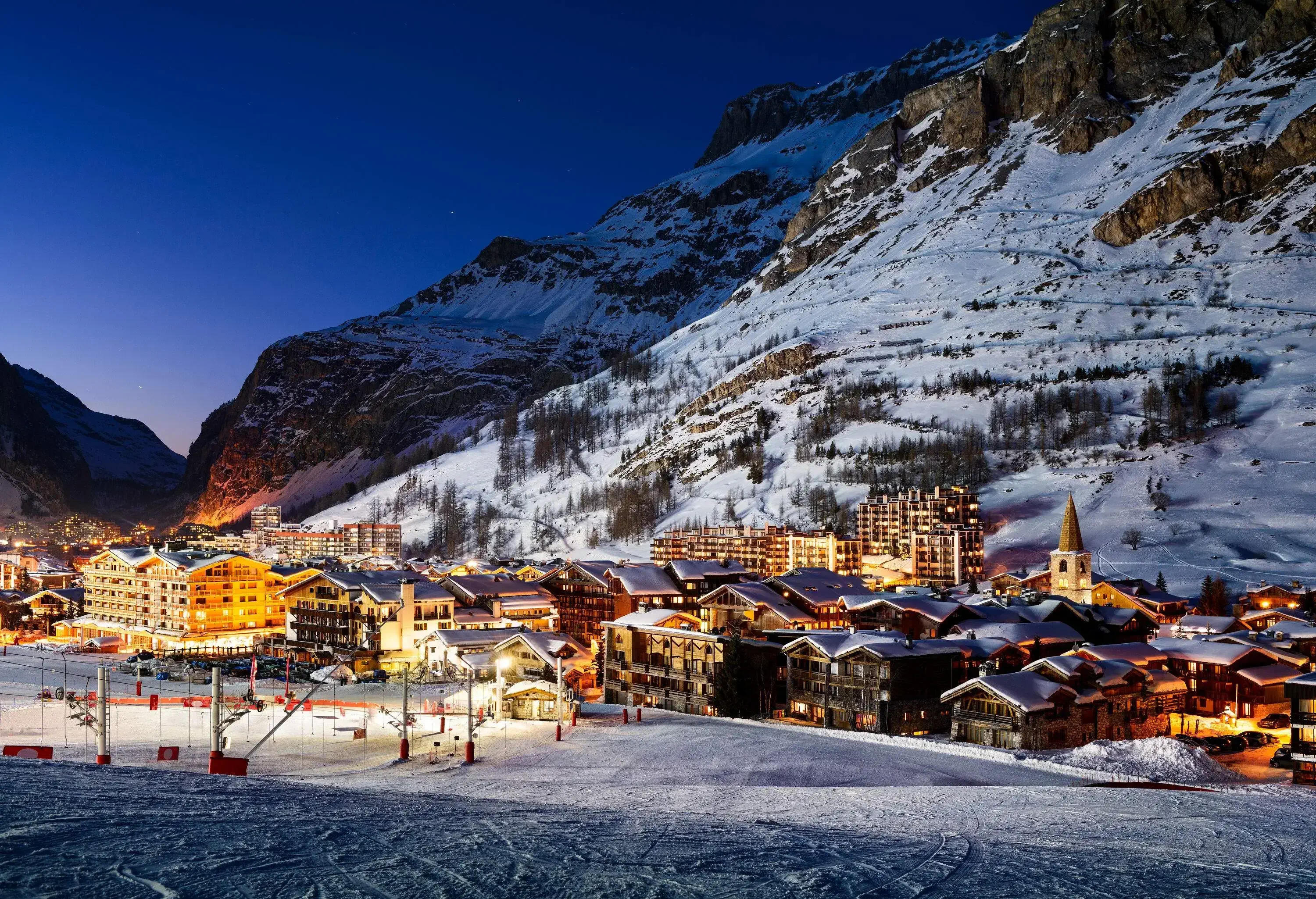 A picturesque snow-covered hillside community with bright lights and gondolas.