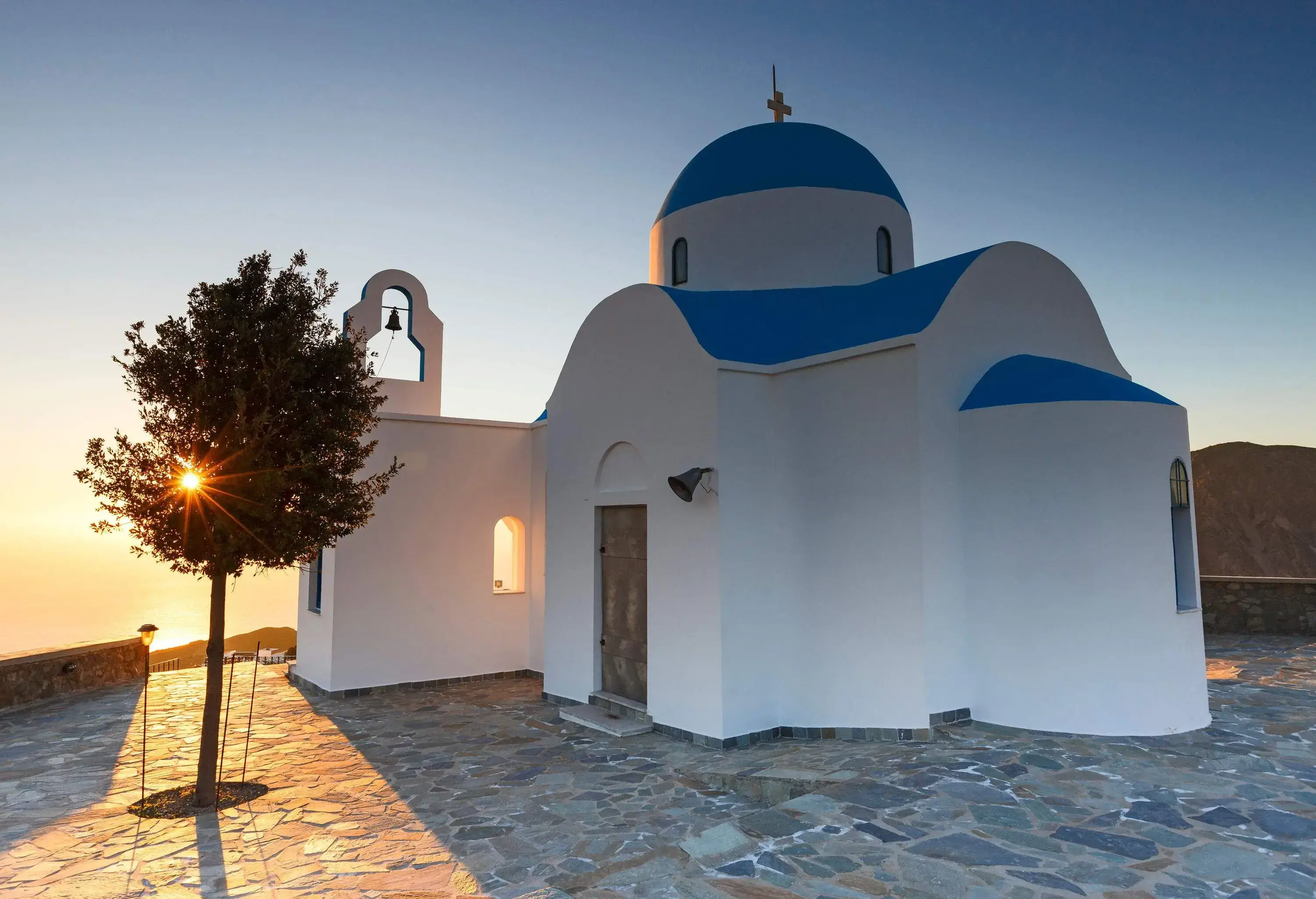 A pristine white chapel with blue-painted roofs and a bell gable at sunset.