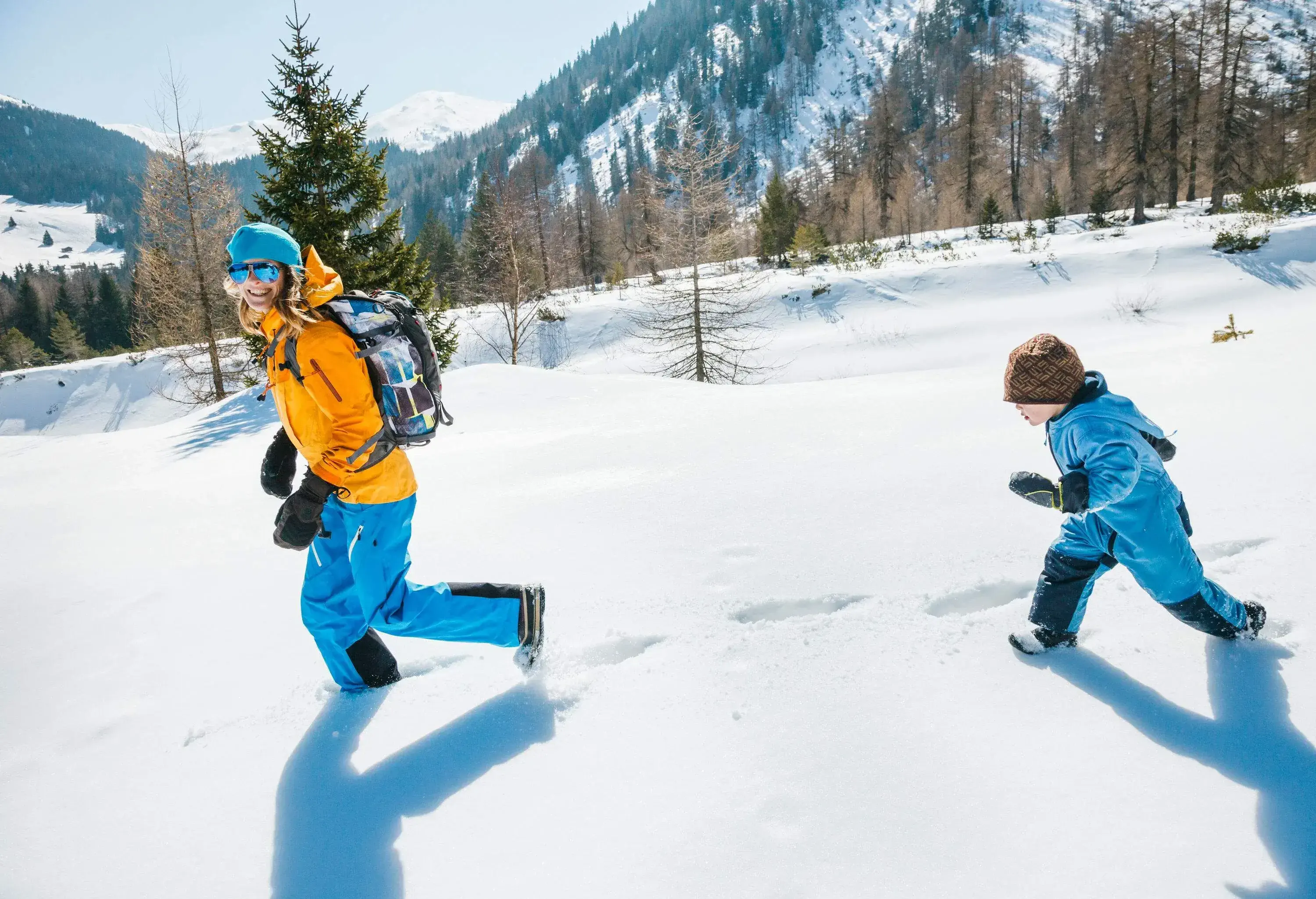 A woman and a kid in winter clothing left behind snow footprints while running through a deep snow field.