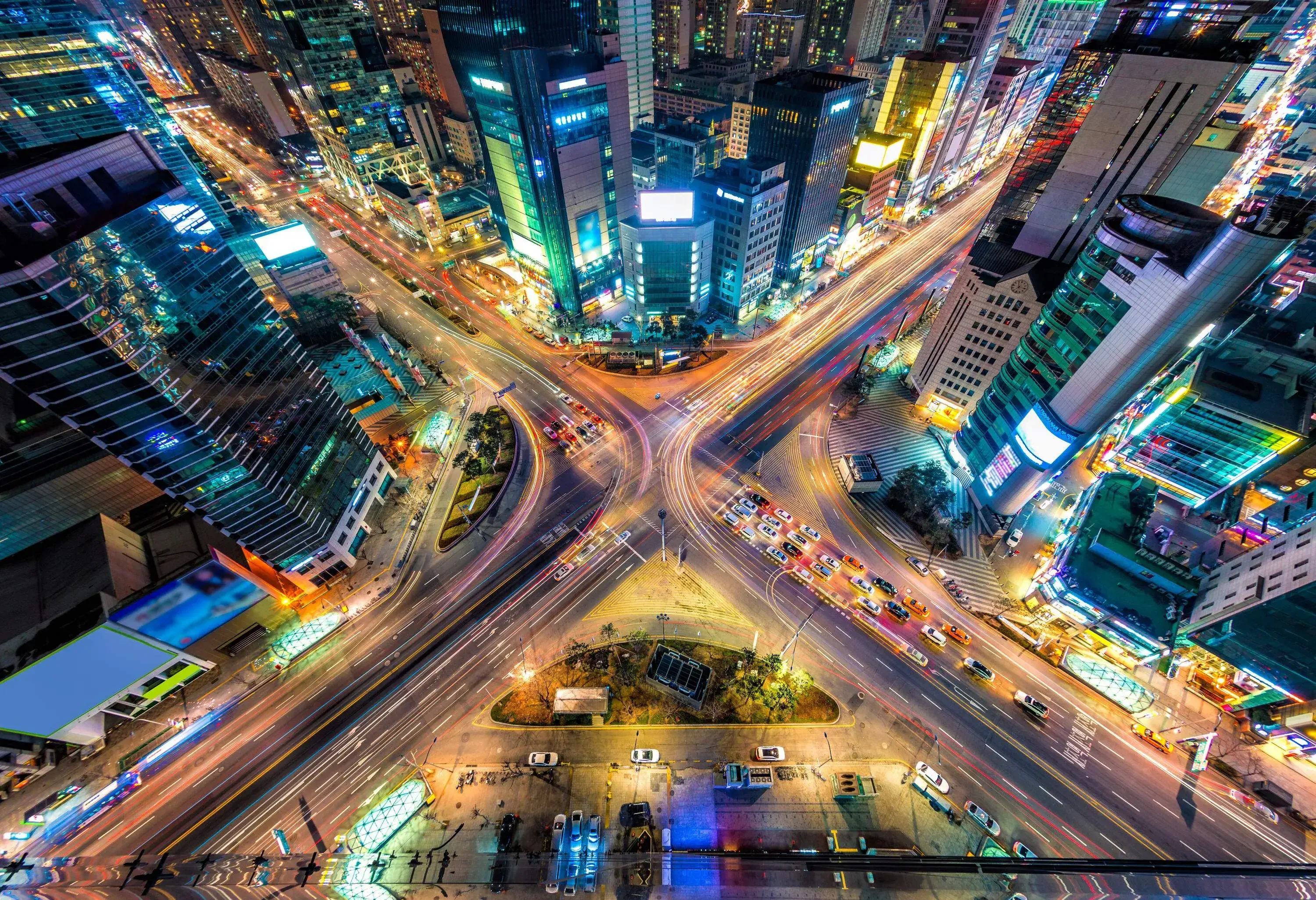 Top view of a bustling intersection surrounded by tall modern buildings brightly lit at night.