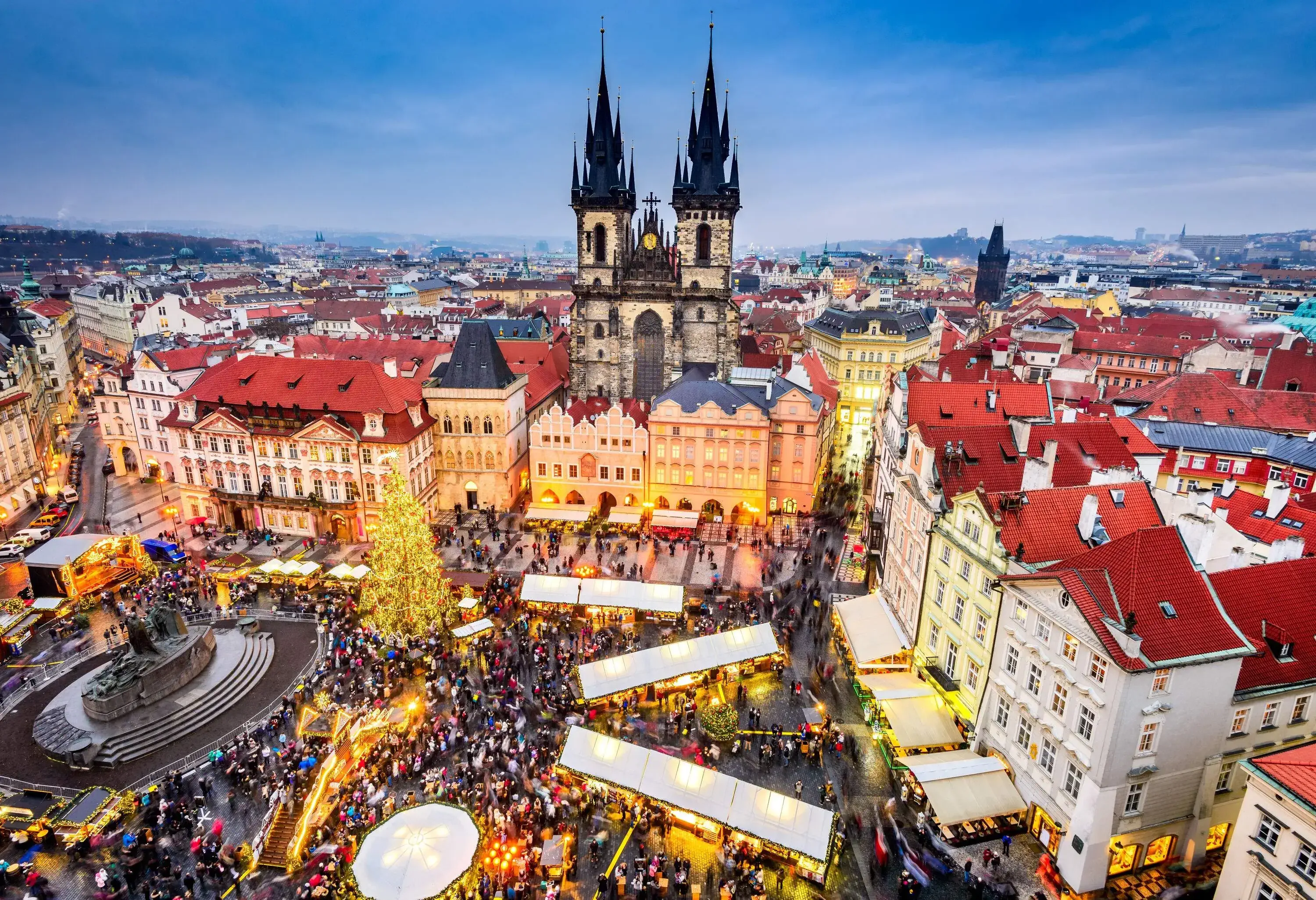 A busy market square with a huge monument and a lit up Christmas tree at one end.