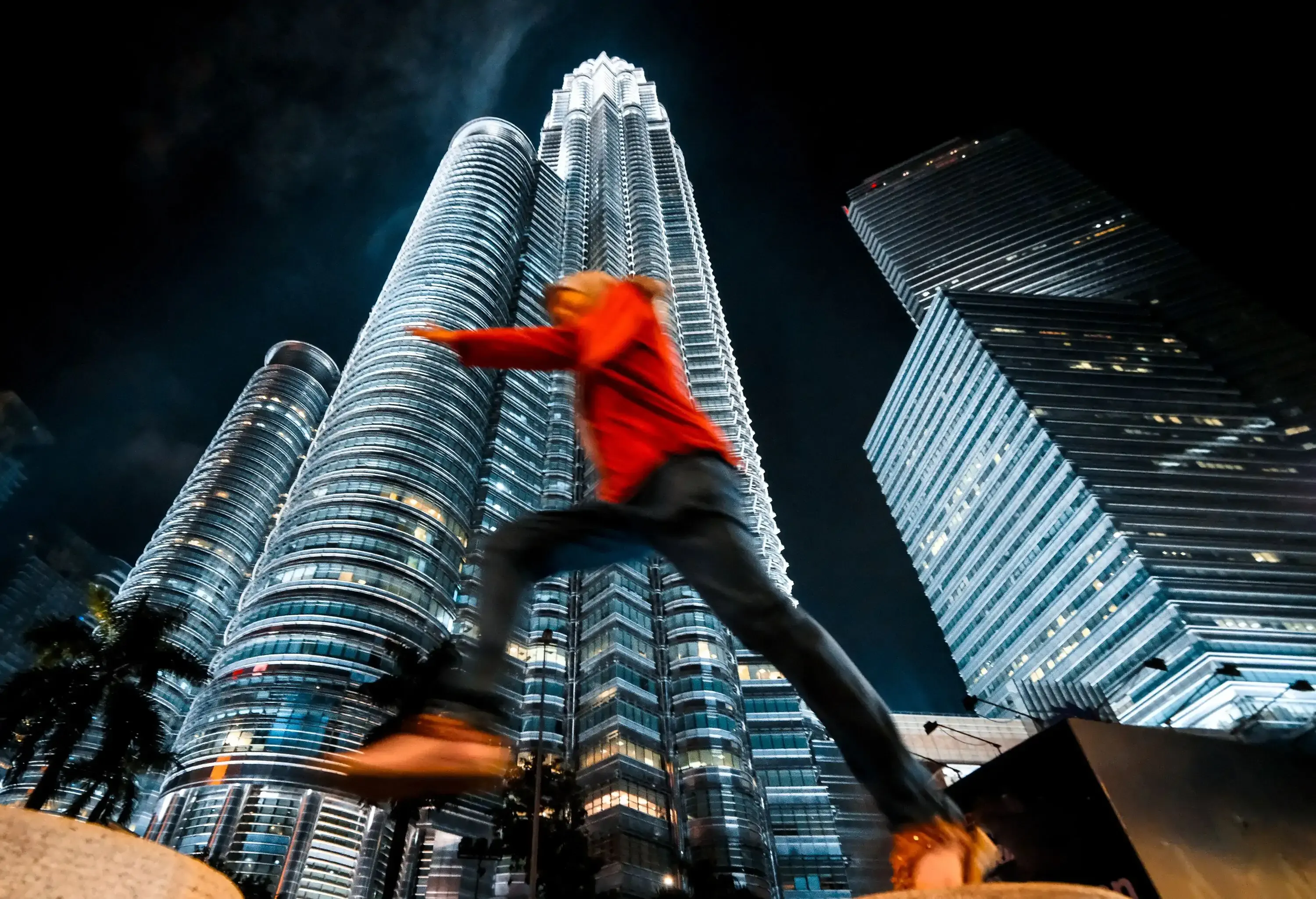 A man leaping off against the brightly lit twin tower in the backdrop.