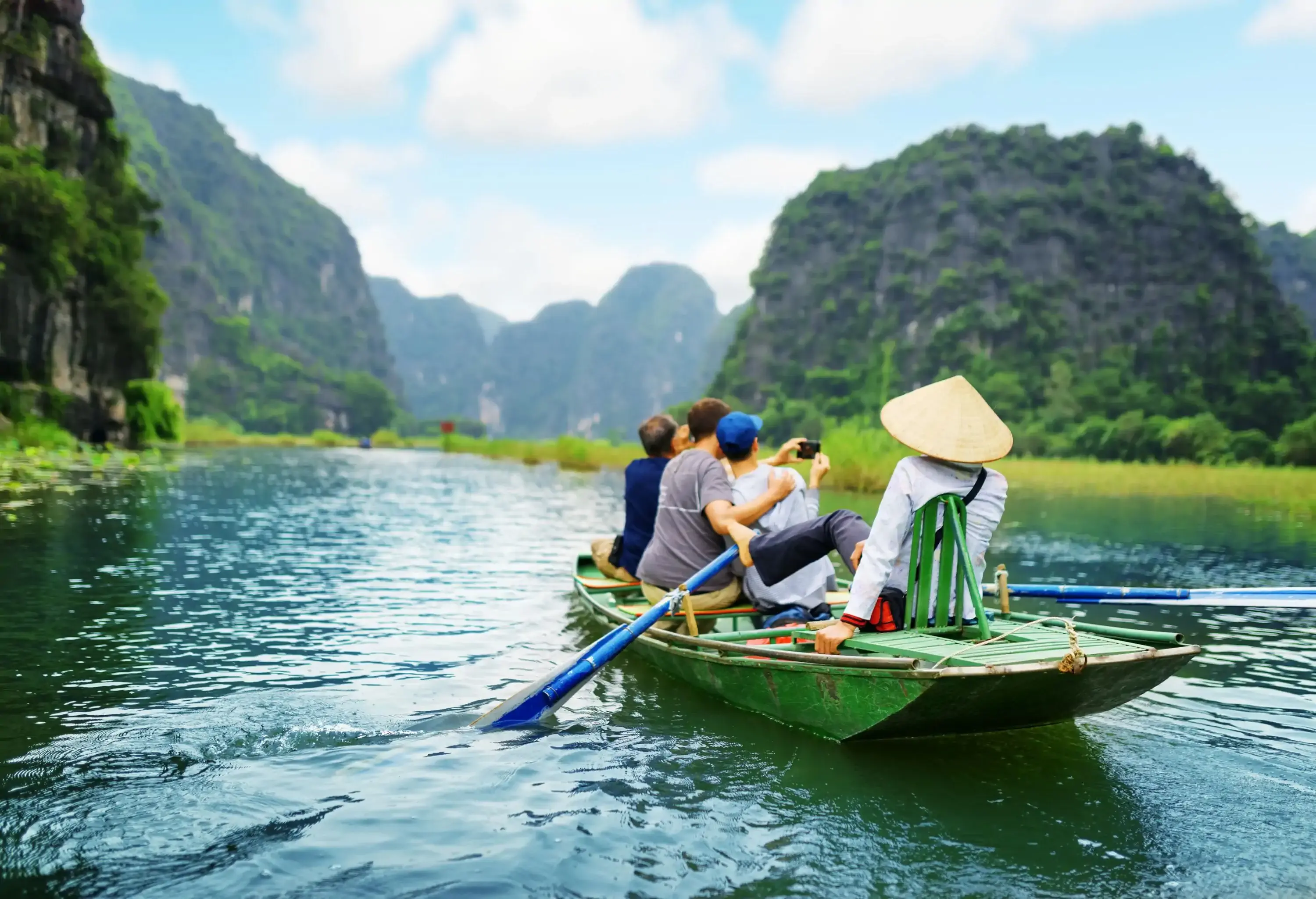 Tourists riding in a boat down the river, photographing the magnificent rock formations in the background, while the rower propels the canoe with her feet.