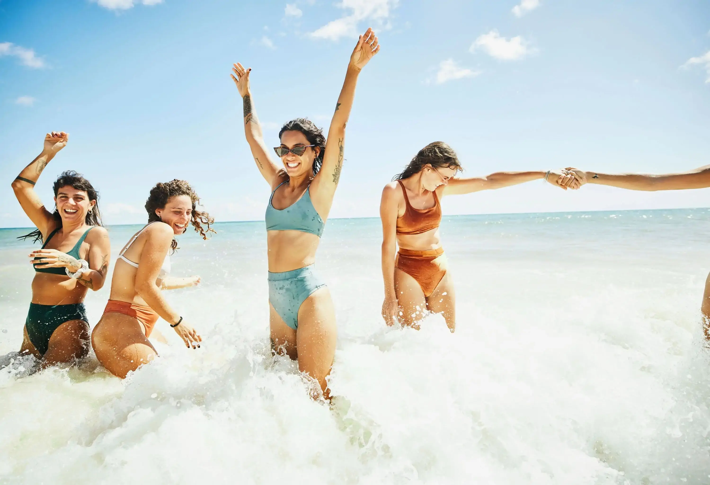 Wide shot of laughing and smiling female friends playing in surf at tropical beach