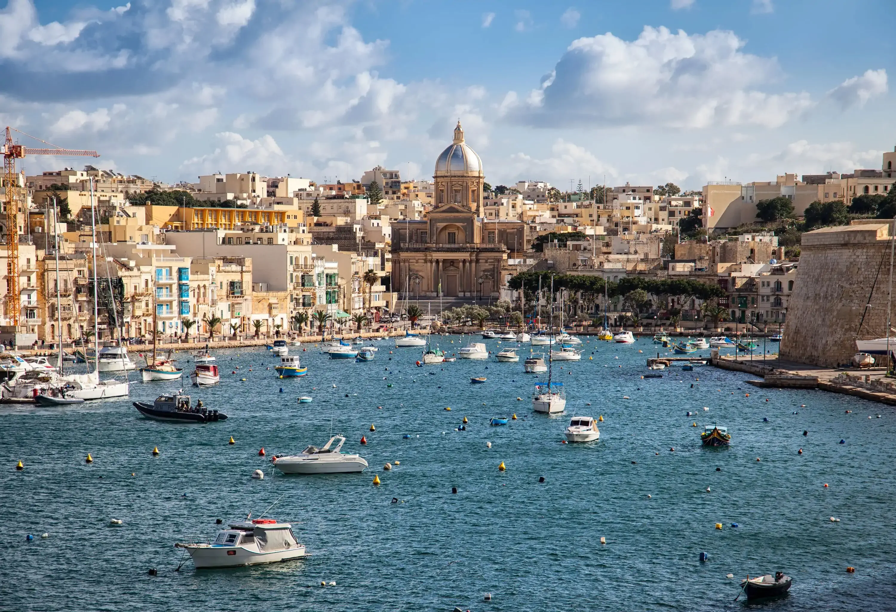 A coastal town with the sea littered with buoys and sailboats and the shore surrounded by historic buildings.