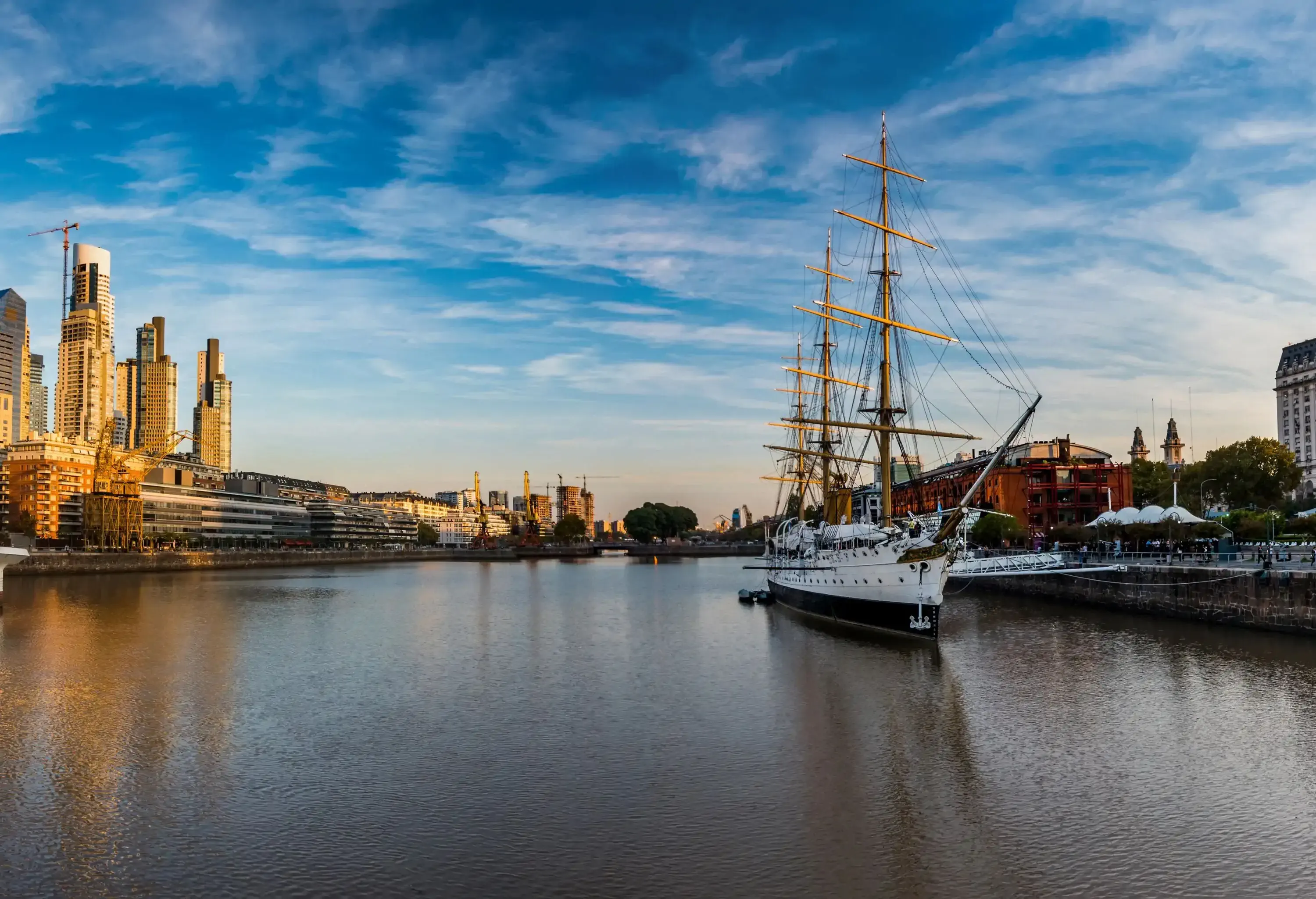 A magnificent museum ship, moored gracefully along the river, while towering buildings on both banks stand as a testament to the vibrant cityscape.