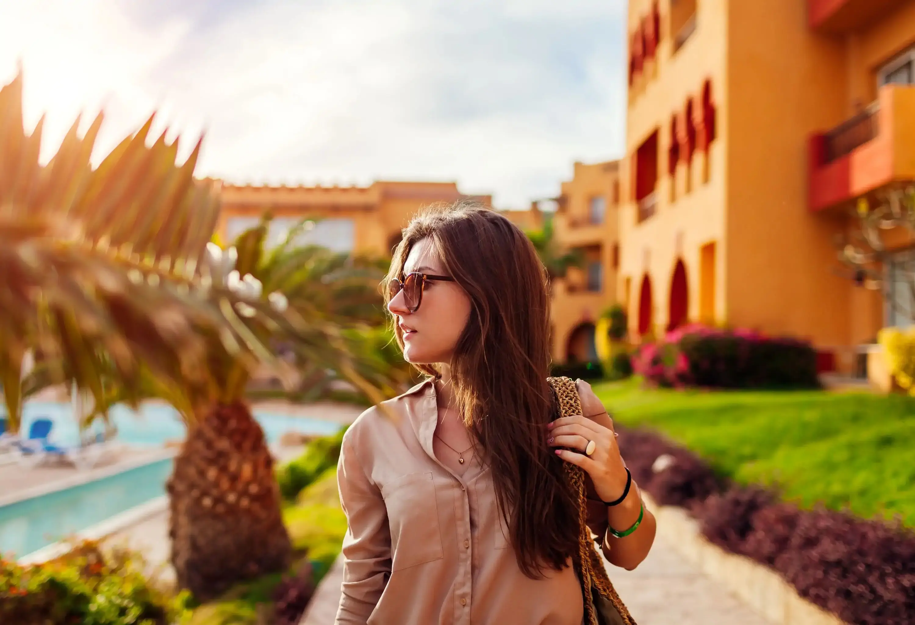 Portrait of young stylish woman walking by tropical palms in hotel yard in Egypt. Summer vacation on exotic resort