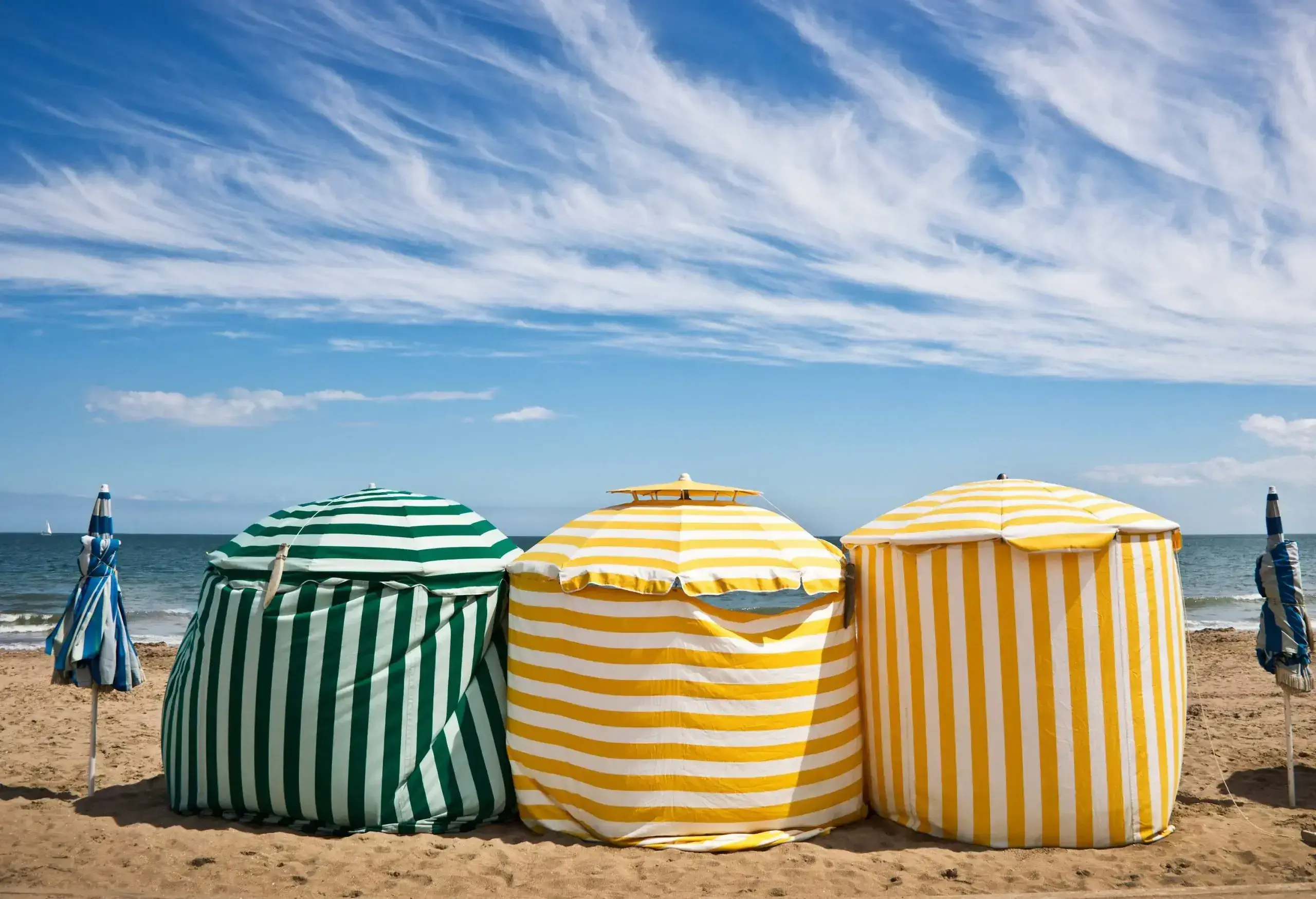 Colourful striped tents standing on golden sand along the shore.
