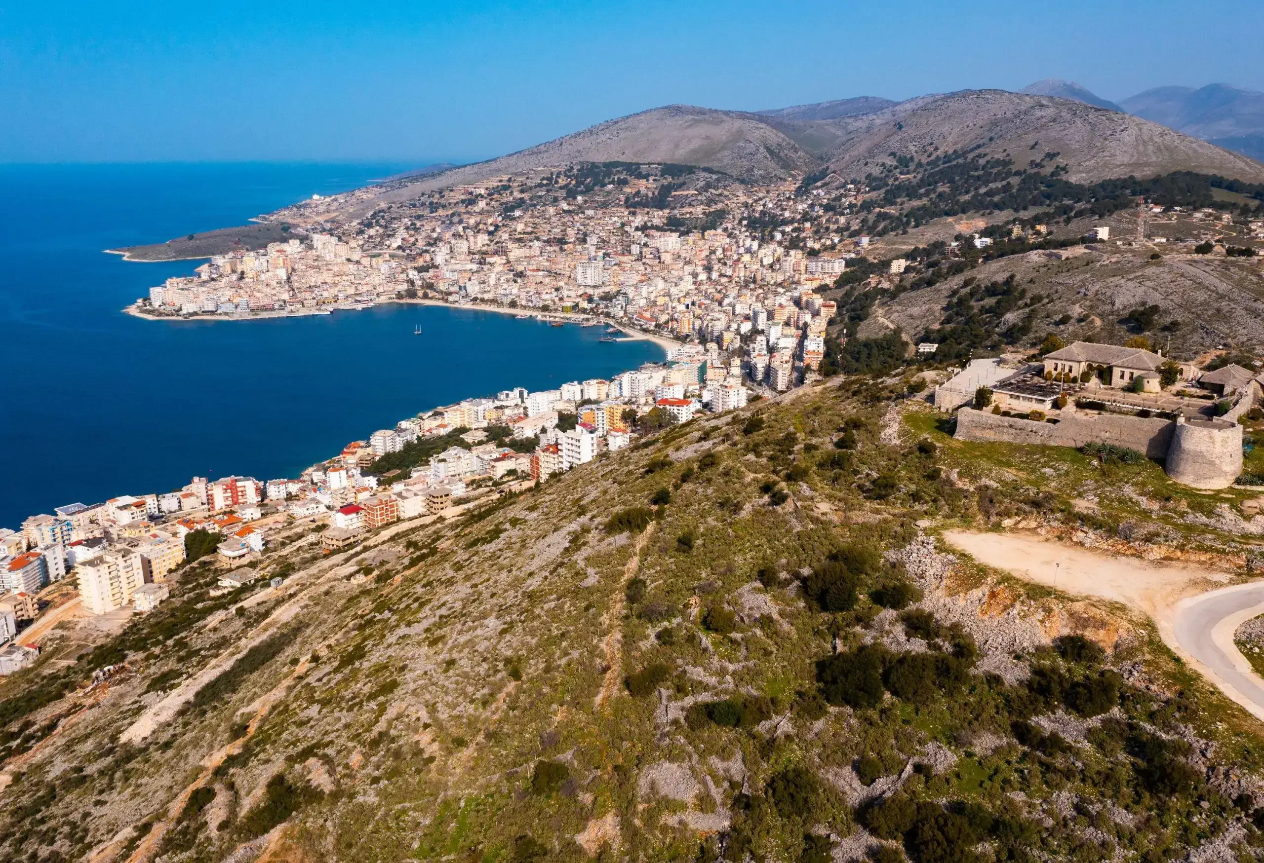 A ruined castle with an imposing round tower on the hilltop overlooking the tranquil blue sea bounded by a whitewashed village.
