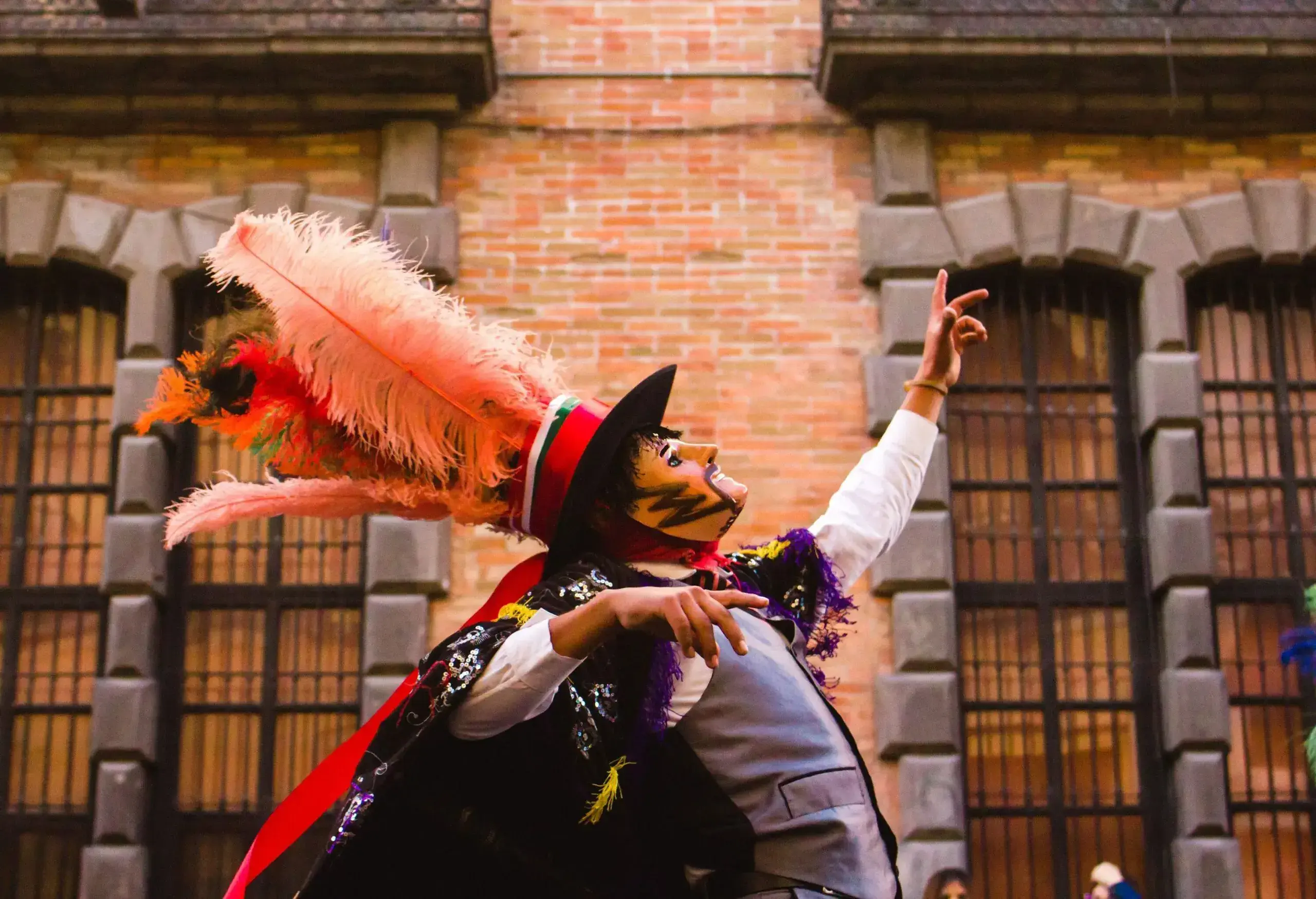 A dancing man in a traditional folk costume with a colourful cape, mask, and a hat adorned with vibrant feathers.