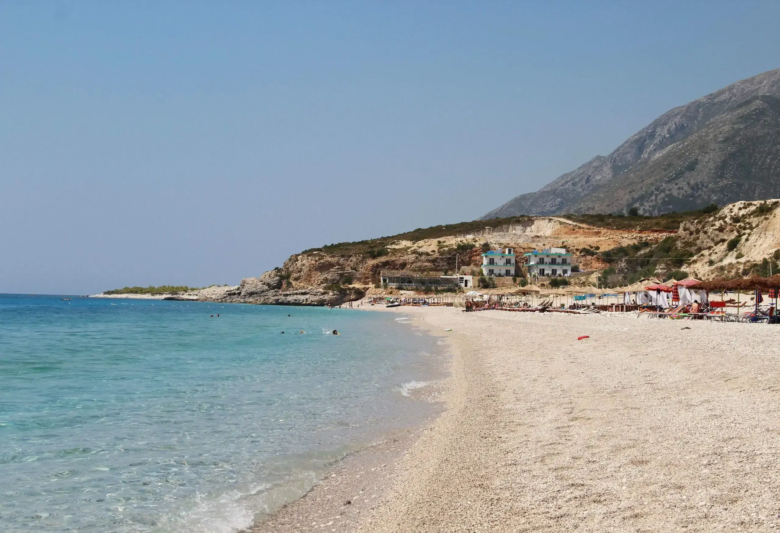 A small sandy beach lined with huts alongside the steep hills.