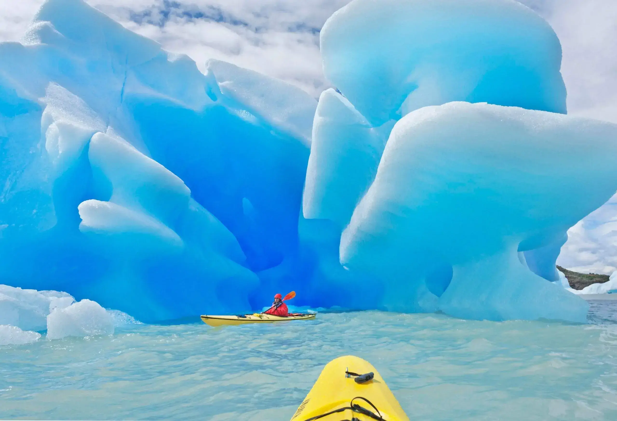 A person is paddling a yellow kayak alongside the massive icebergs.