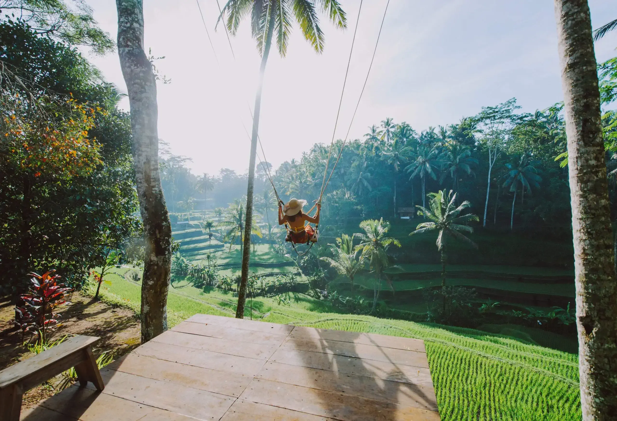 A woman in a wide-brimmed hat sat on a huge swing above the vast rice fields.