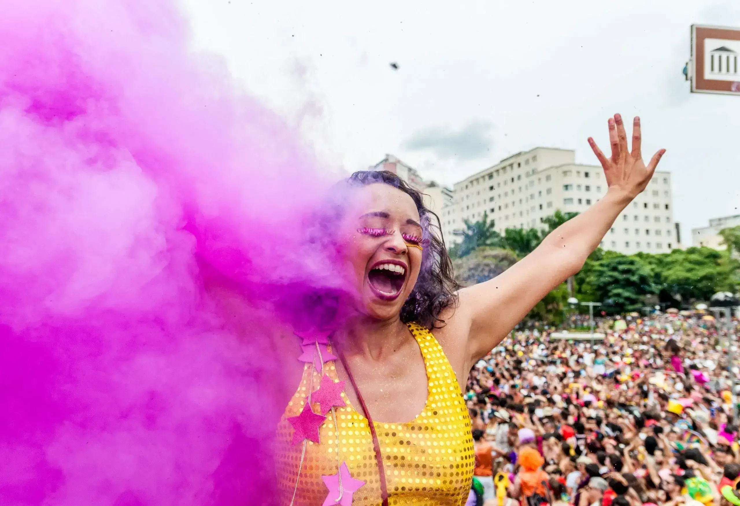 A woman in great joy raised her hands along the purple smoke against the crowd in the background.