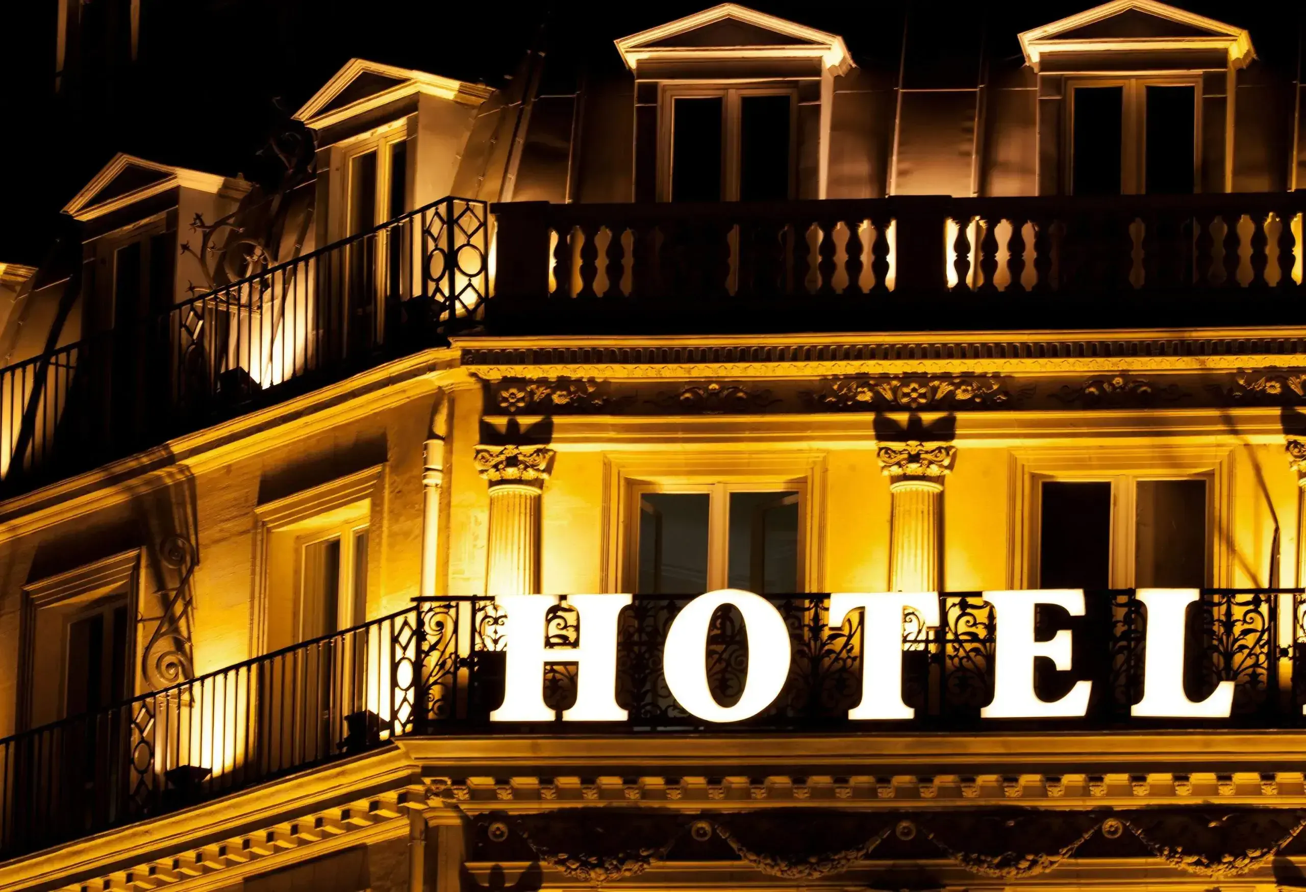 Illuminated hotel signage hangs on a balcony grill.