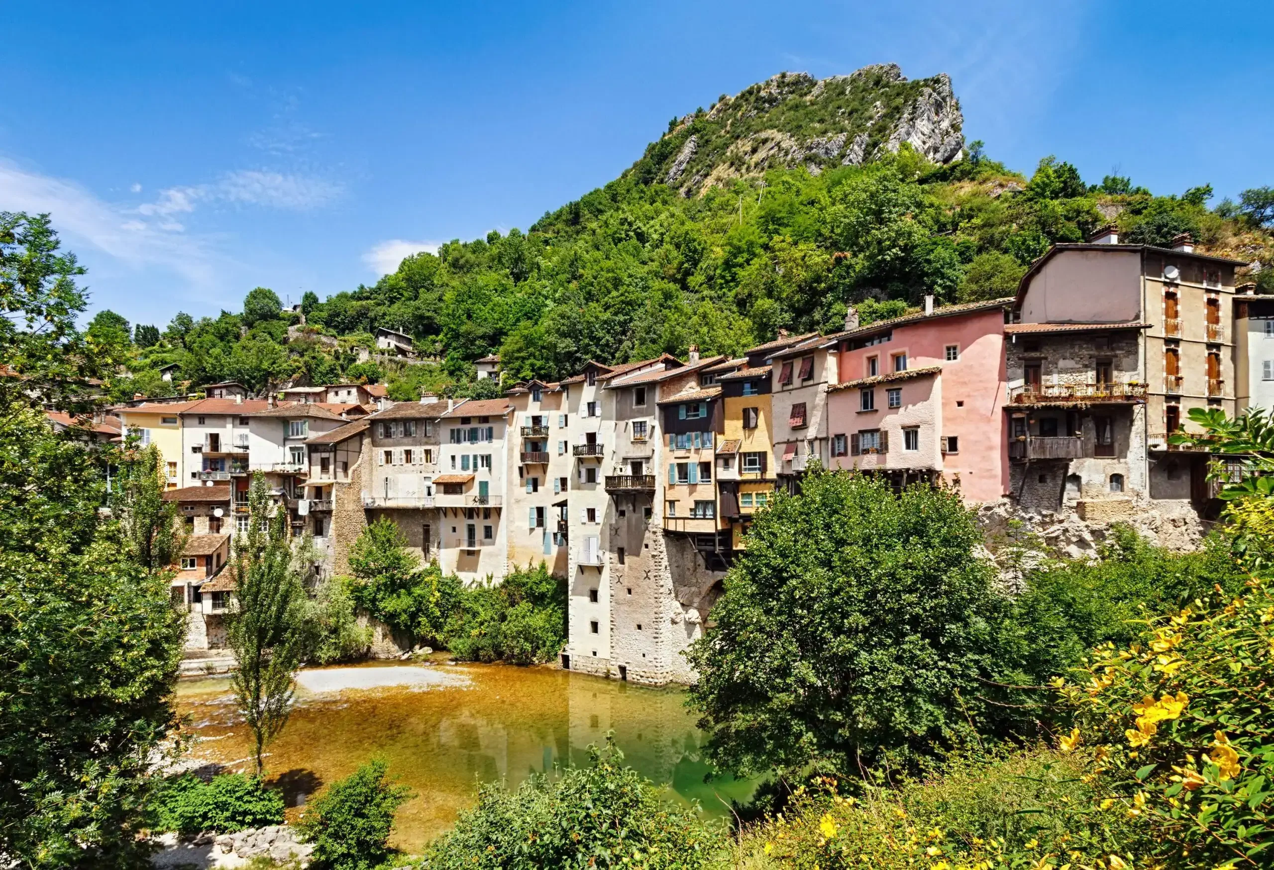 A scenic and charming settlement perched on the side of a cliff overgrown with vegetation next to a wet area.