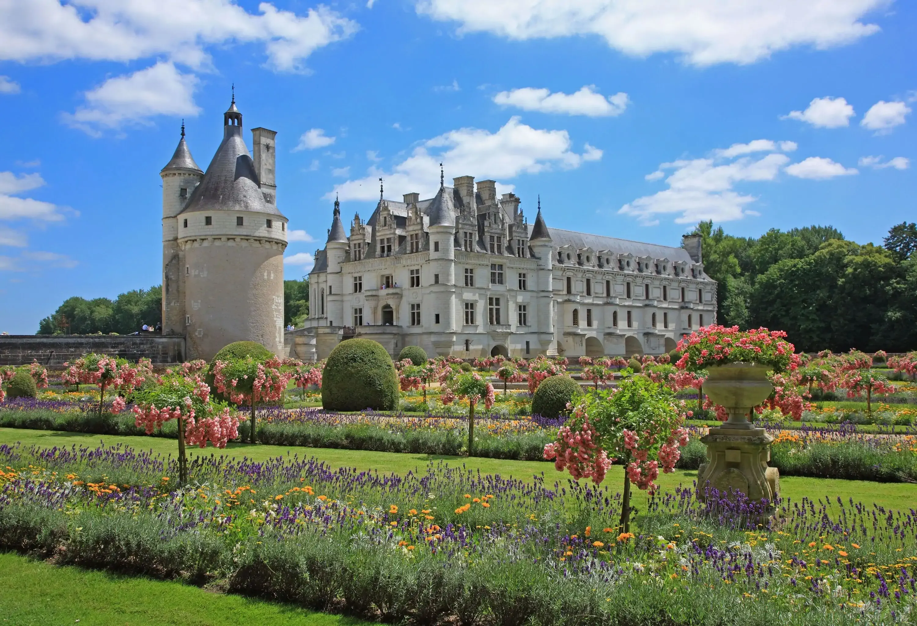 A broad garden with a well-kept lawn and colourful flowers in front of a castle.