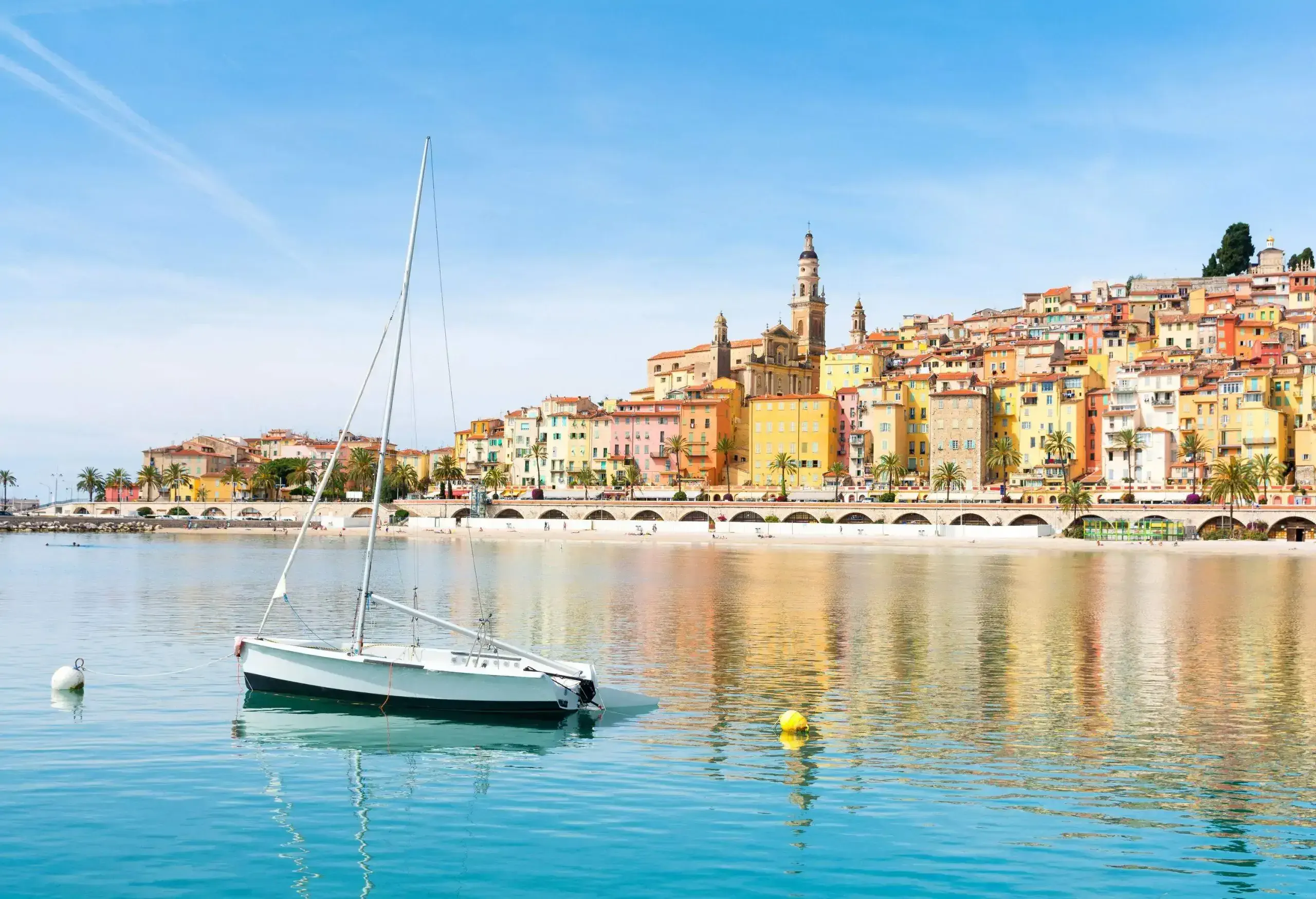 A small boat in the ocean overlooking the colourful coastal cityscape with classic buildings against the cloudy blue sky.