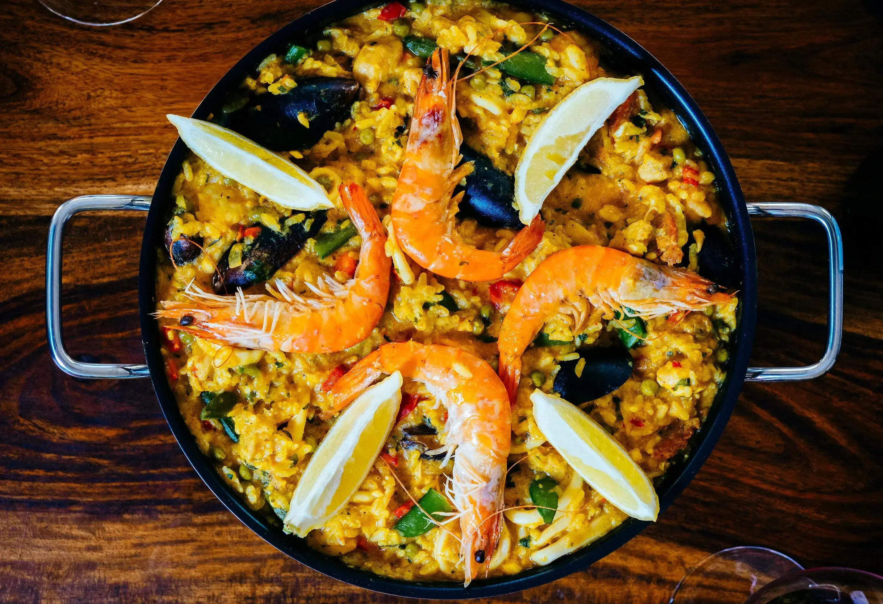 A dish with seasoned steamed rice topped with shrimps, mussels, and lemon slices.