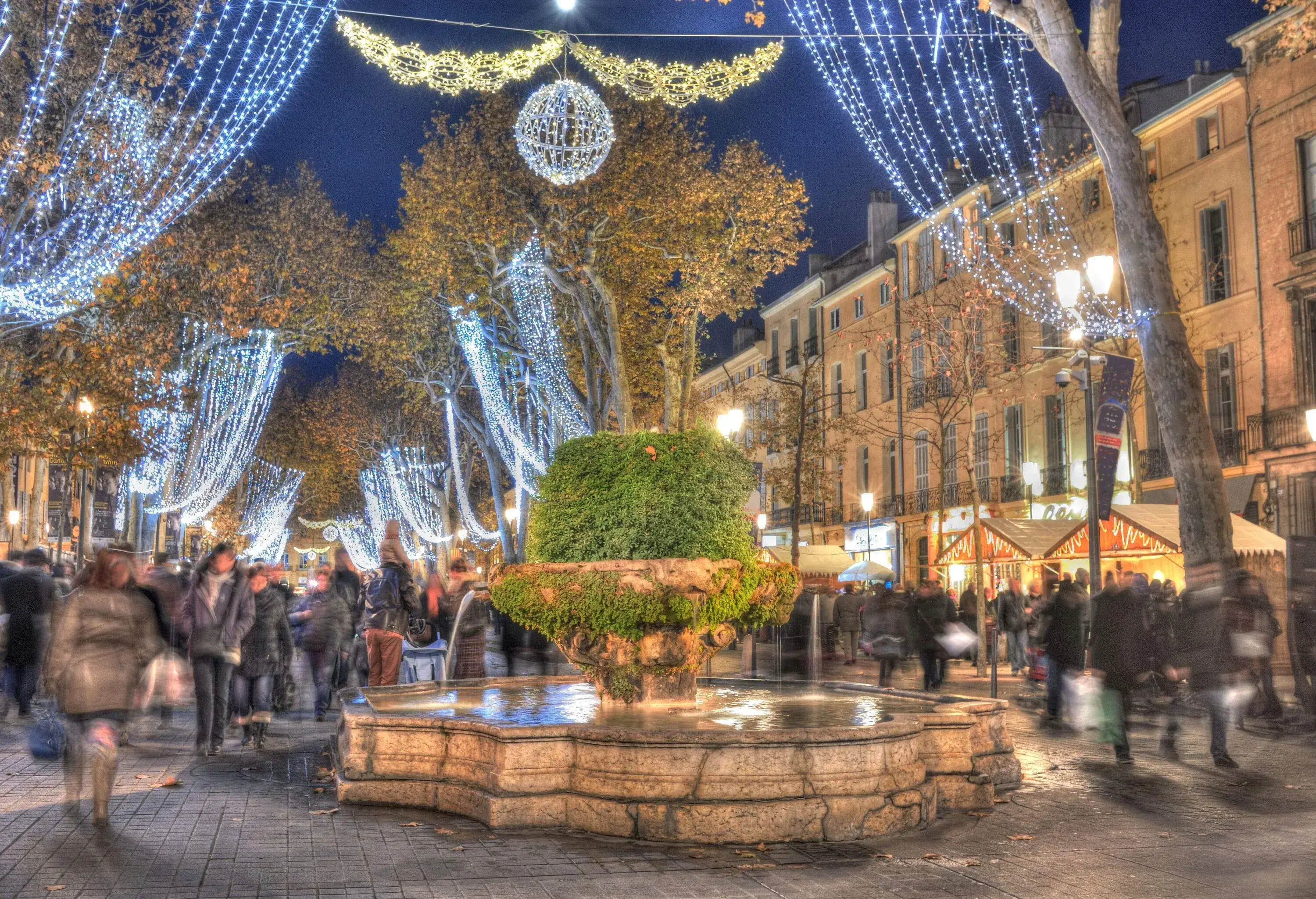 A busy Christmas market with string lights strung from the trees.