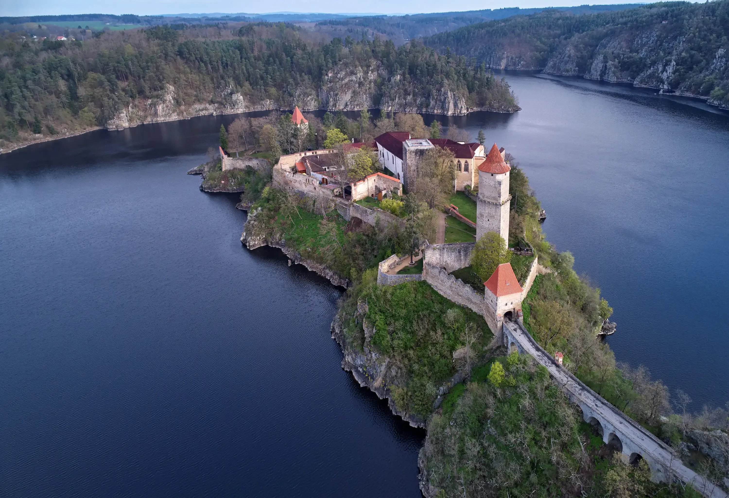 A castle with a tall watchtower set on a promontory that spans a tranquil body of water.