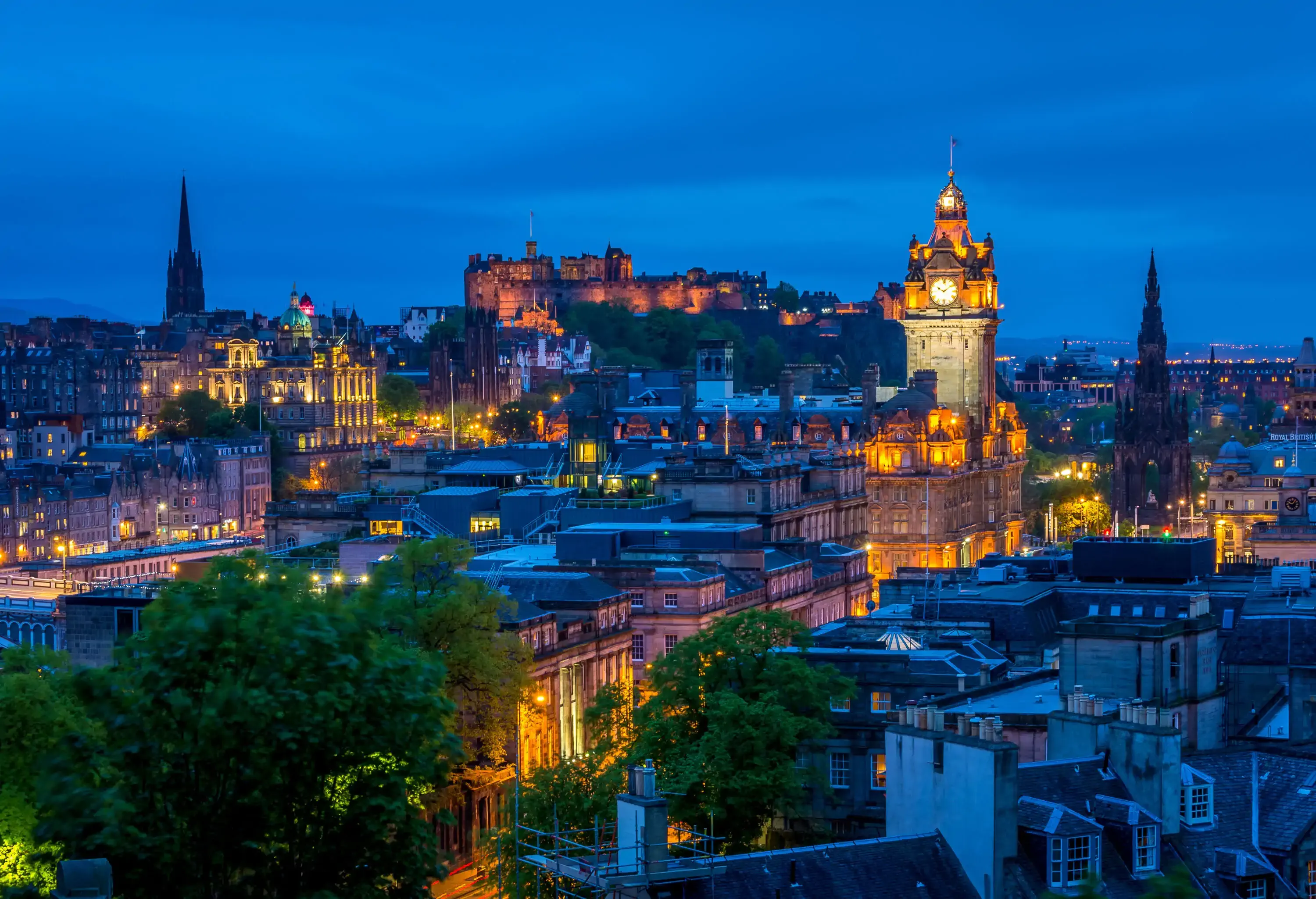 A radiant old cityscape featuring classic and elegant buildings, with an 11th-century castle crowning a hill in the background against the twilight sky.