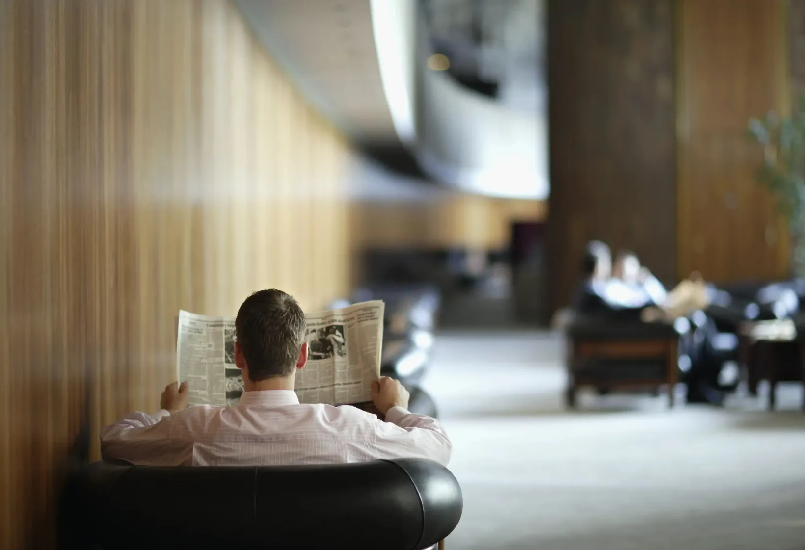 A man sitting in a cozy lobby armchair, engrossed in reading a newspaper, with warm ambient lighting creating a relaxed atmosphere