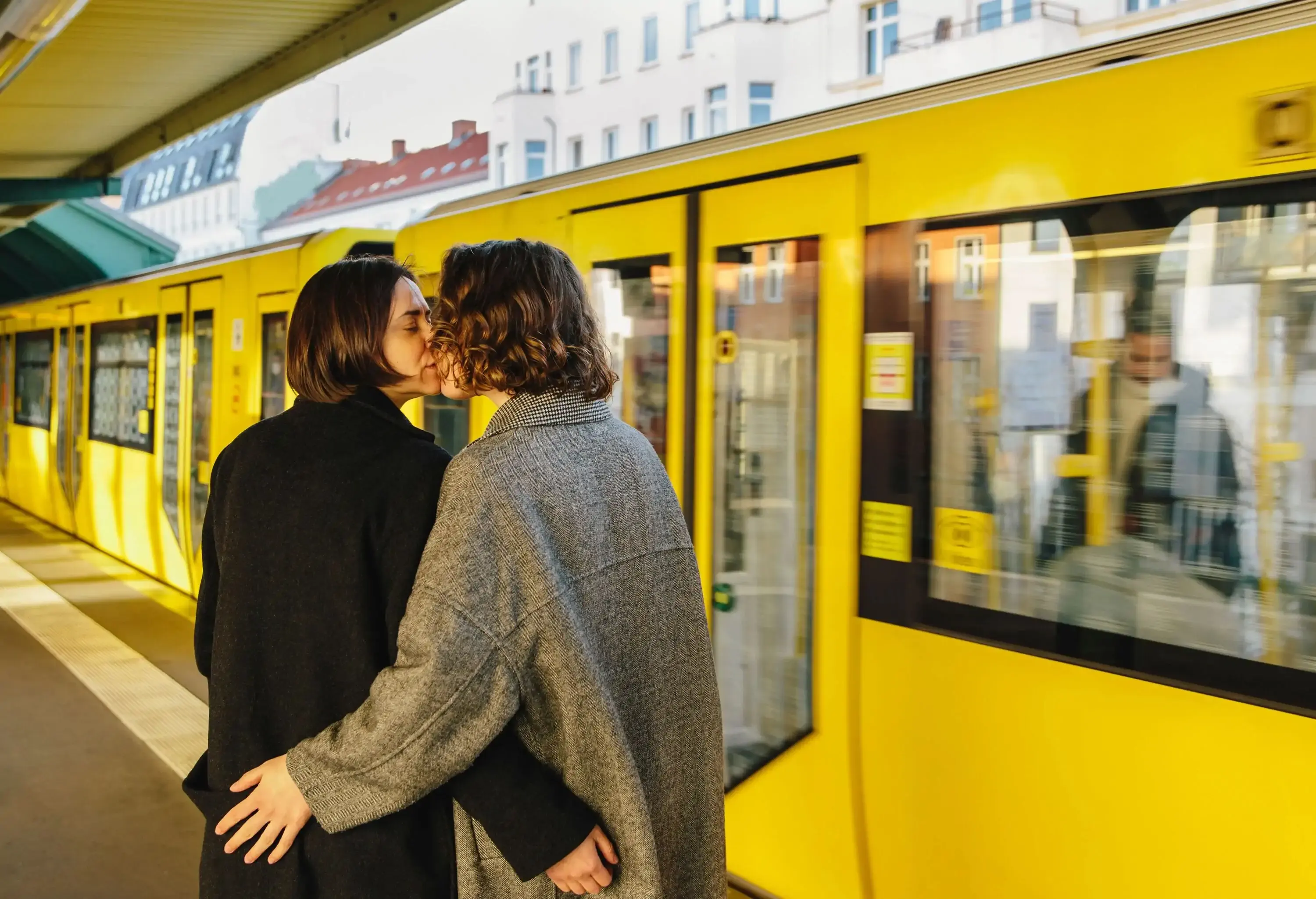 Lesbian couple kissing while standing by yellow train at railroad station