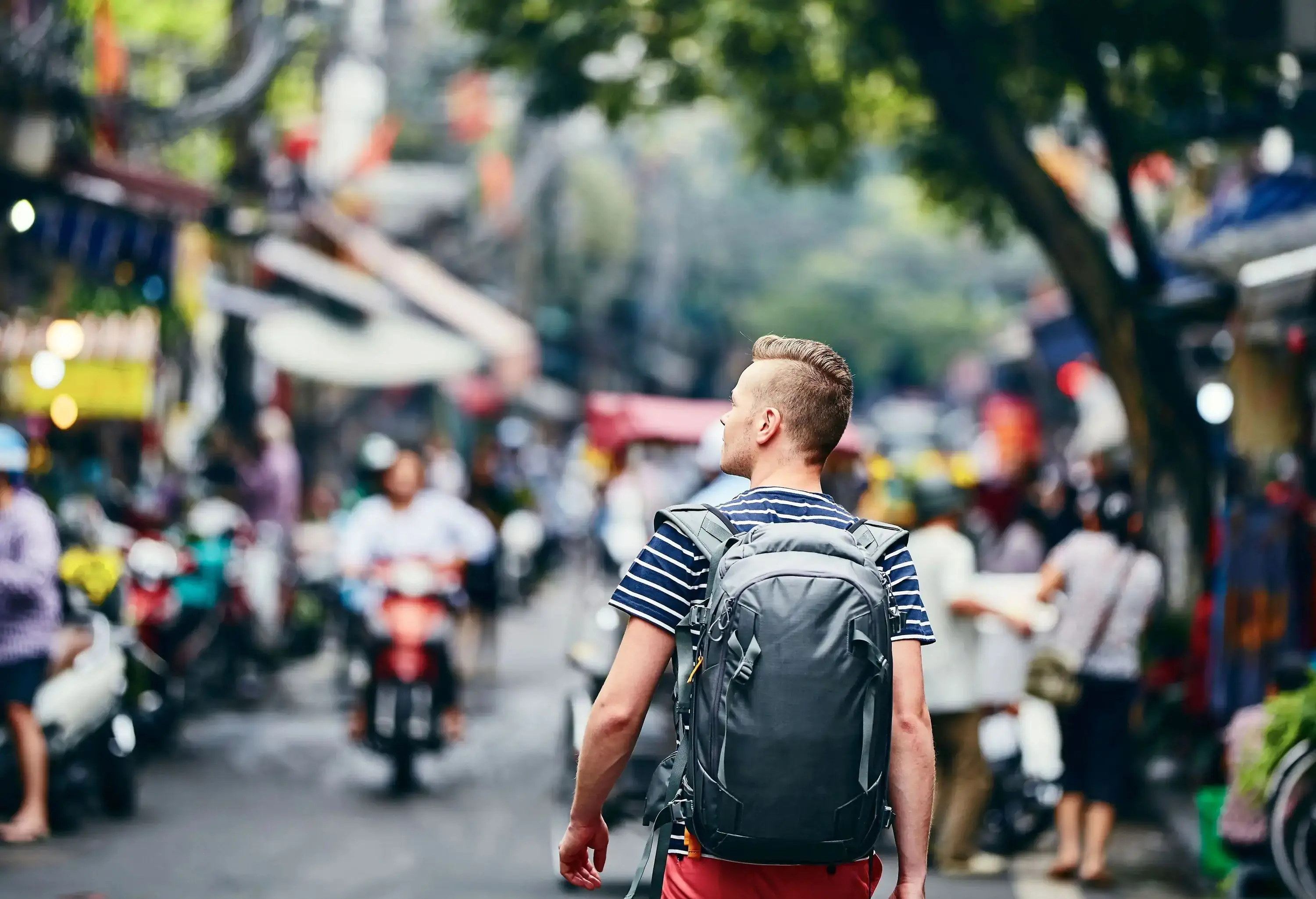 A man in a striped shirt and backpack strolls a busy street.