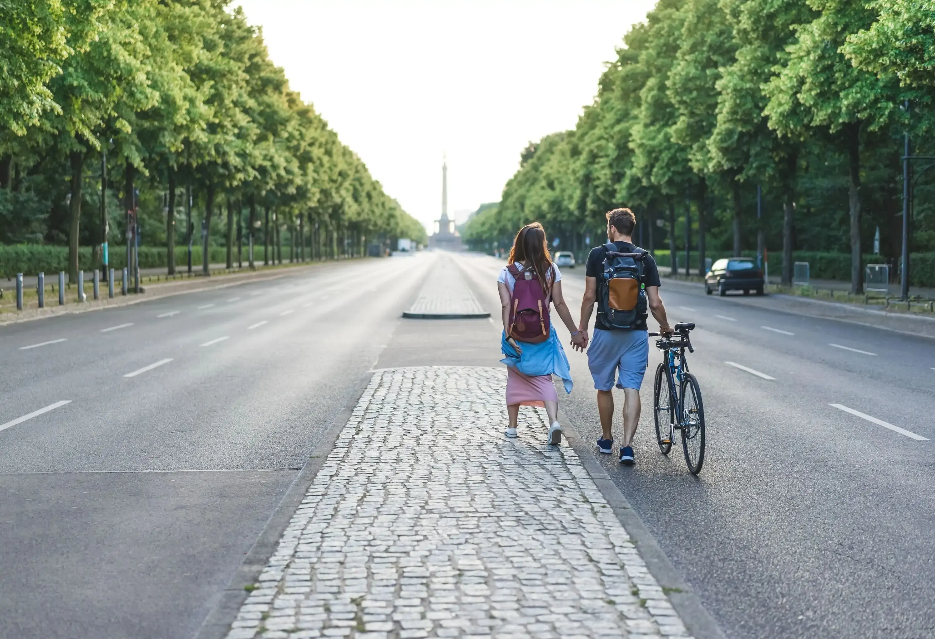 rear view of couple of tourists with bicycle walking at street in Berlin, Germany ; Shutterstock ID 1130146838