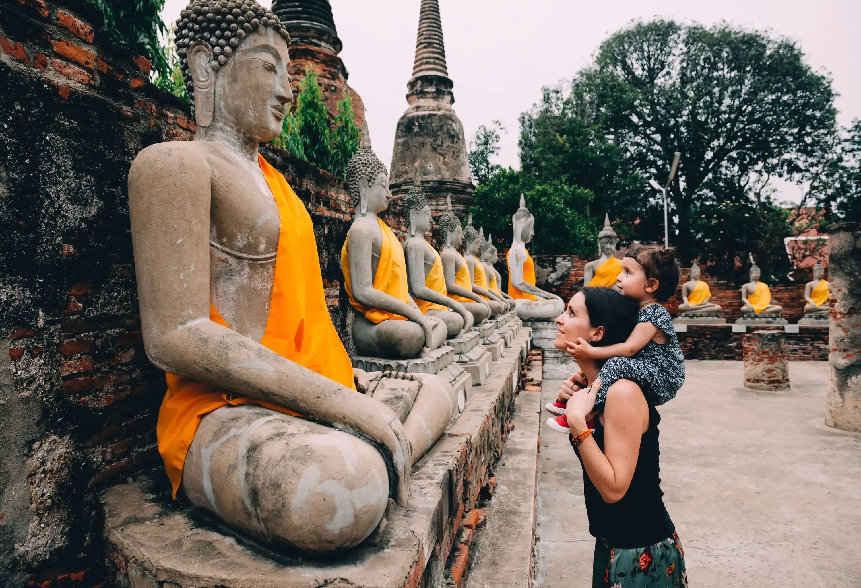 Mother with daughter on her shoulders gazing at a row of Buddha statues