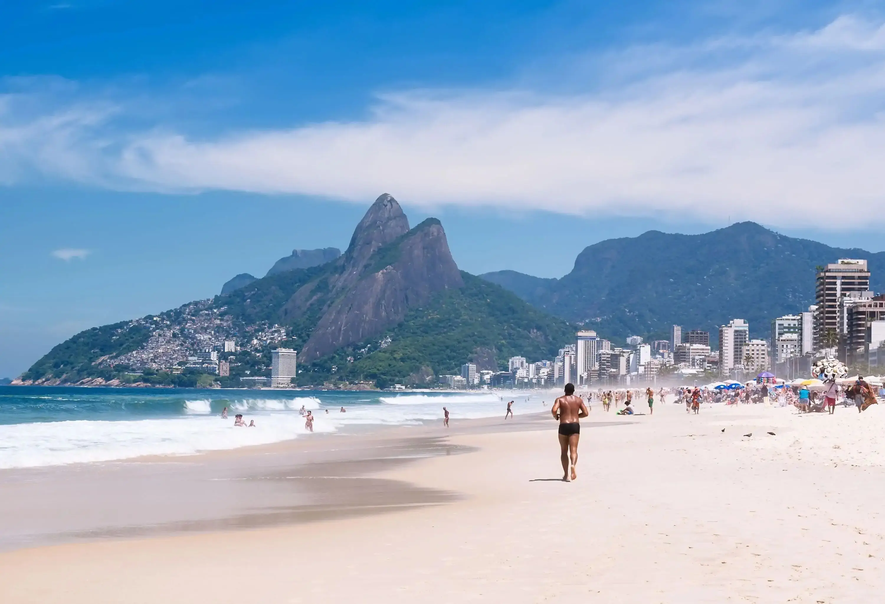 A wide white sandy beach with skyscrapers and dramatic mountain range in the background
