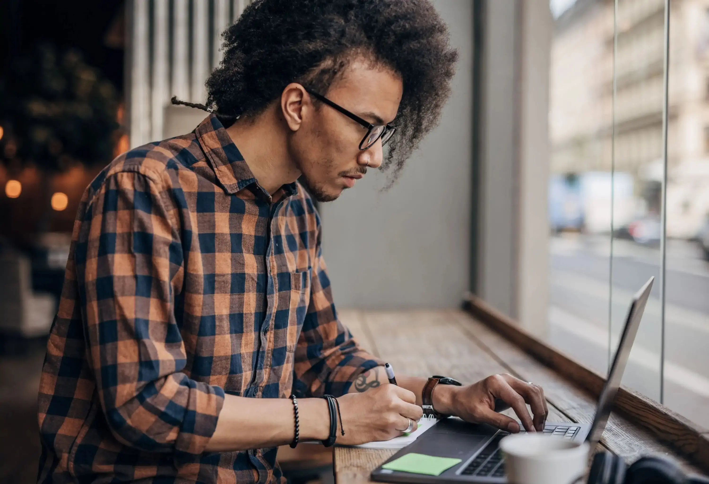 Young hispanic man using laptop in coffee shop writing something