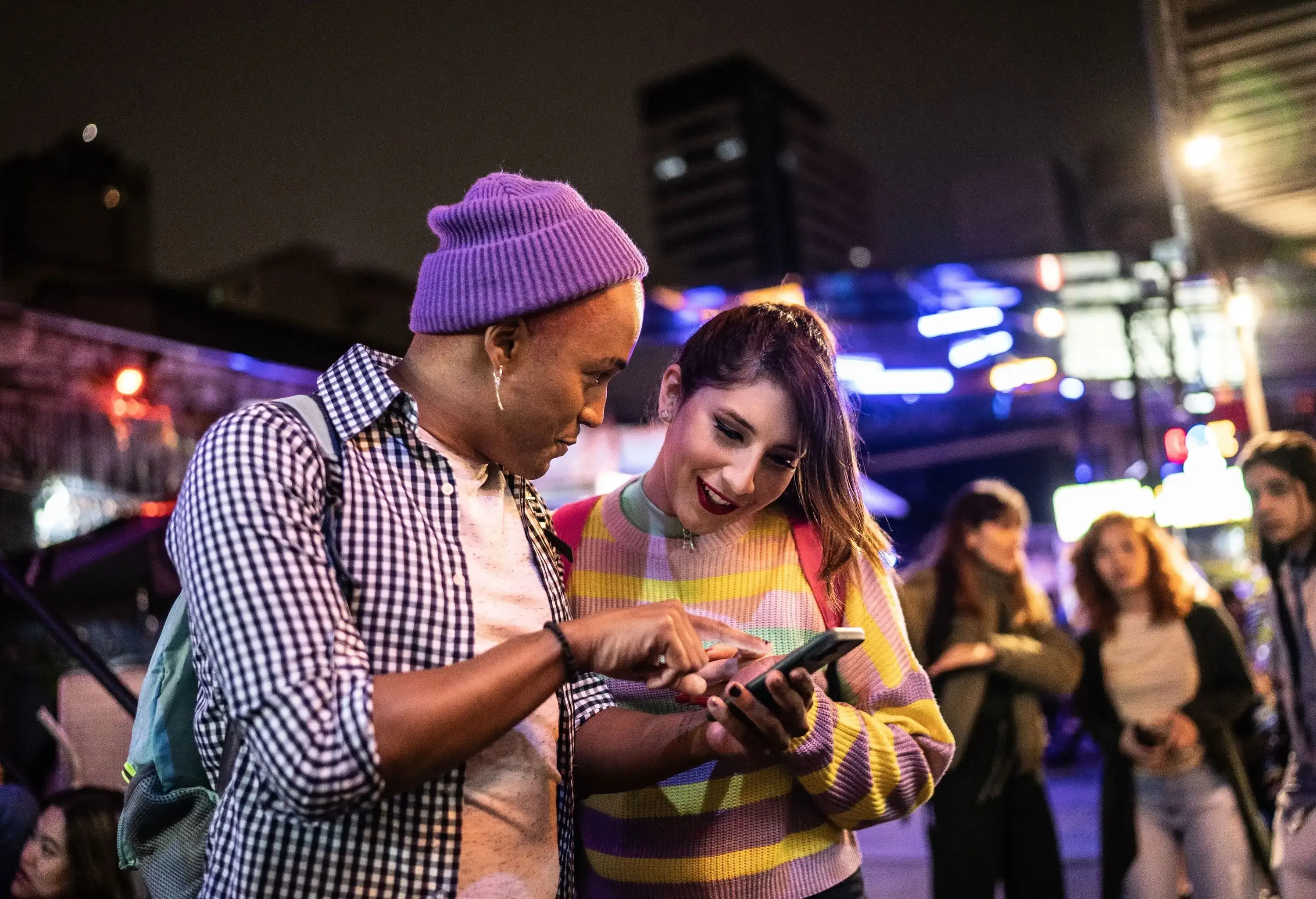 Young couple (or friends) using mobile phone at festival by the night - including a transgender person
