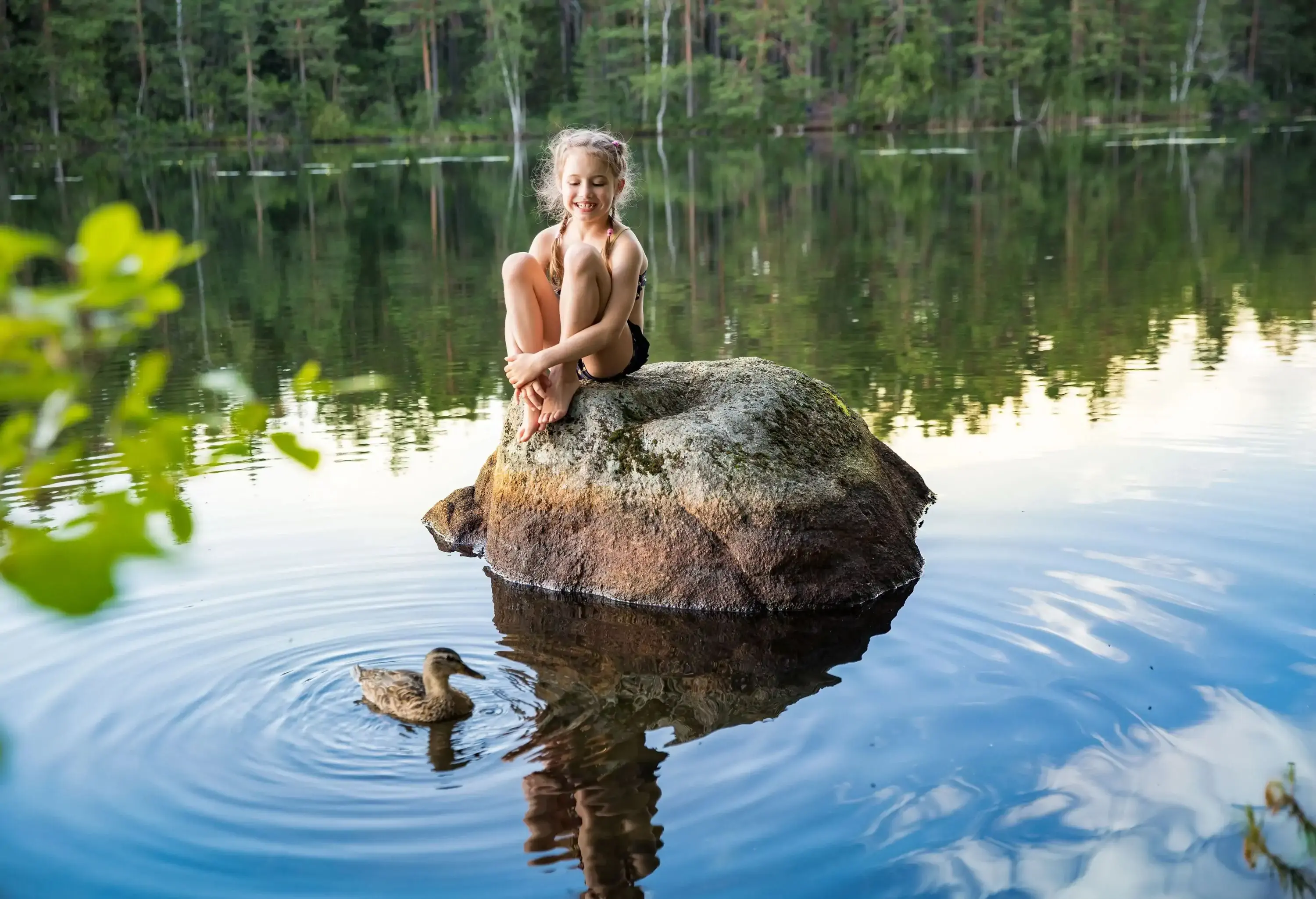 Cute little girl sitting on a rock in lake. Enjoying summer vacation. Child and Nature. Happy isolation concept. Exploring Finland. Scandinavian landscape.